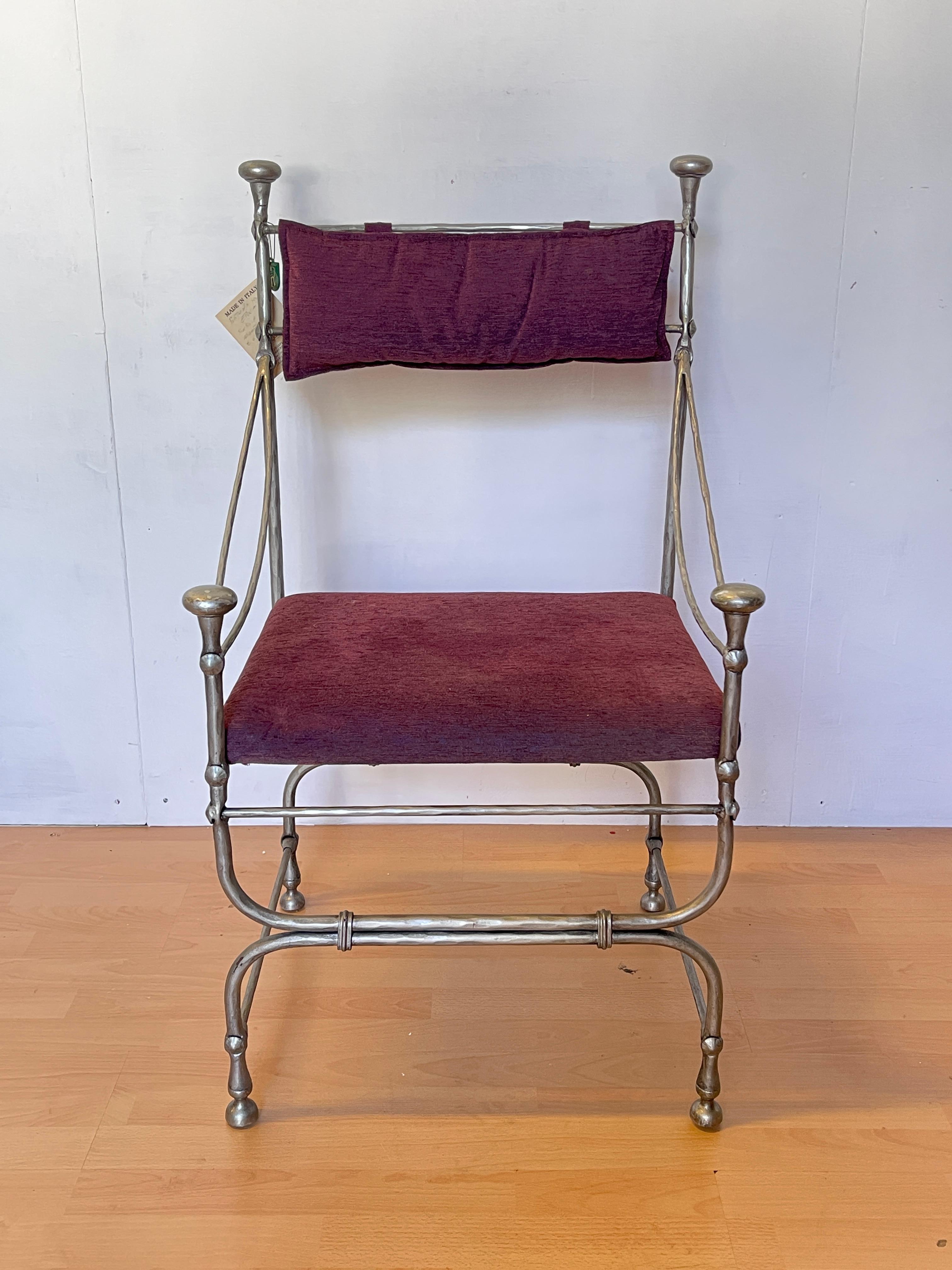 Afascinante sedia artigianale in ferro battuto con seduta e schienale imbottiti in velluto color burdeos. Las líneas sinuosas de la estructura metálica y las texturas decorativas en las esquinas evocan un diseño neoclásico rico en elementos