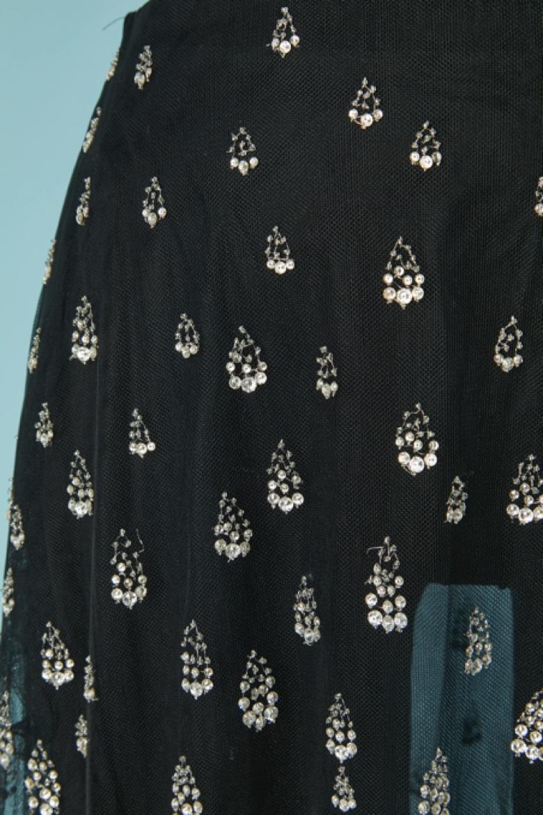 Falda transparente de tul y gasa de seda con adornos de lentejuelas plateadas. La falda se compone de 3 capas (una de tul con lentejuelas, otra de tul liso y otra de gasa de seda lisa). Cremallera invisible y cierre de corchete en el lado