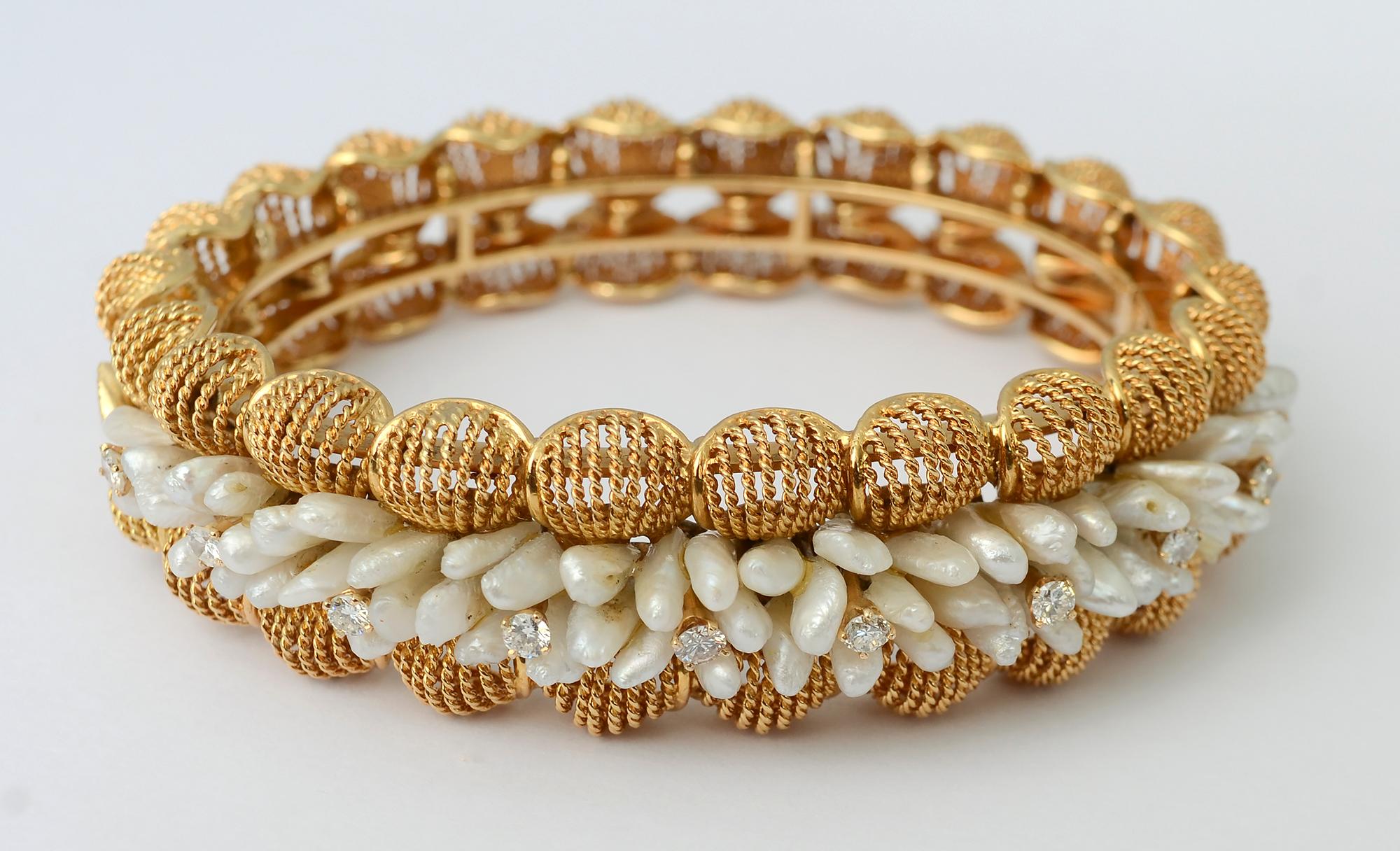 This elegant hinged bangle bracelet is adorned with clusters of seed pearls highlighted with ten diamonds.
The stones are nestled between two rows of round, three dimensional gold links that are fixed in place. Each of the circles is filled with
