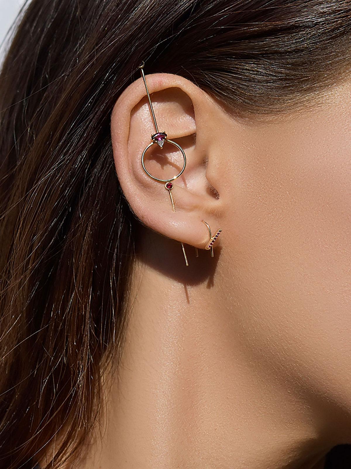 The Seeing Eye Needle Earring is constructed of a needle like gold rod that pierces through your ear lobe and hooks on top. This style is comprised of a circe adorned with gems. 

How to wear it: 
Thread the needle end through the ear lobe piercing