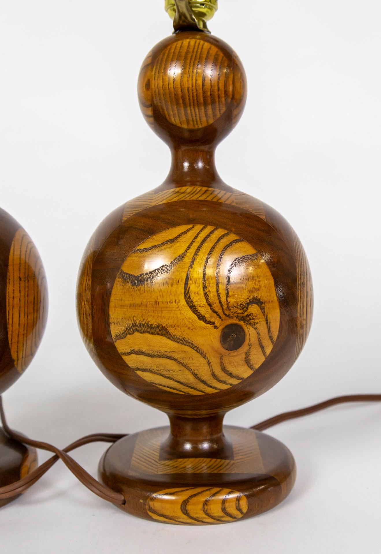 A pair of finely crafted, midcentury table lamps made of segmented wood- a composite of various kinds of wood combined in blocks to reveal a complex design after being turned on a lathe. The heavy, hardwood lamps have a wavy, bulbous, modern shape