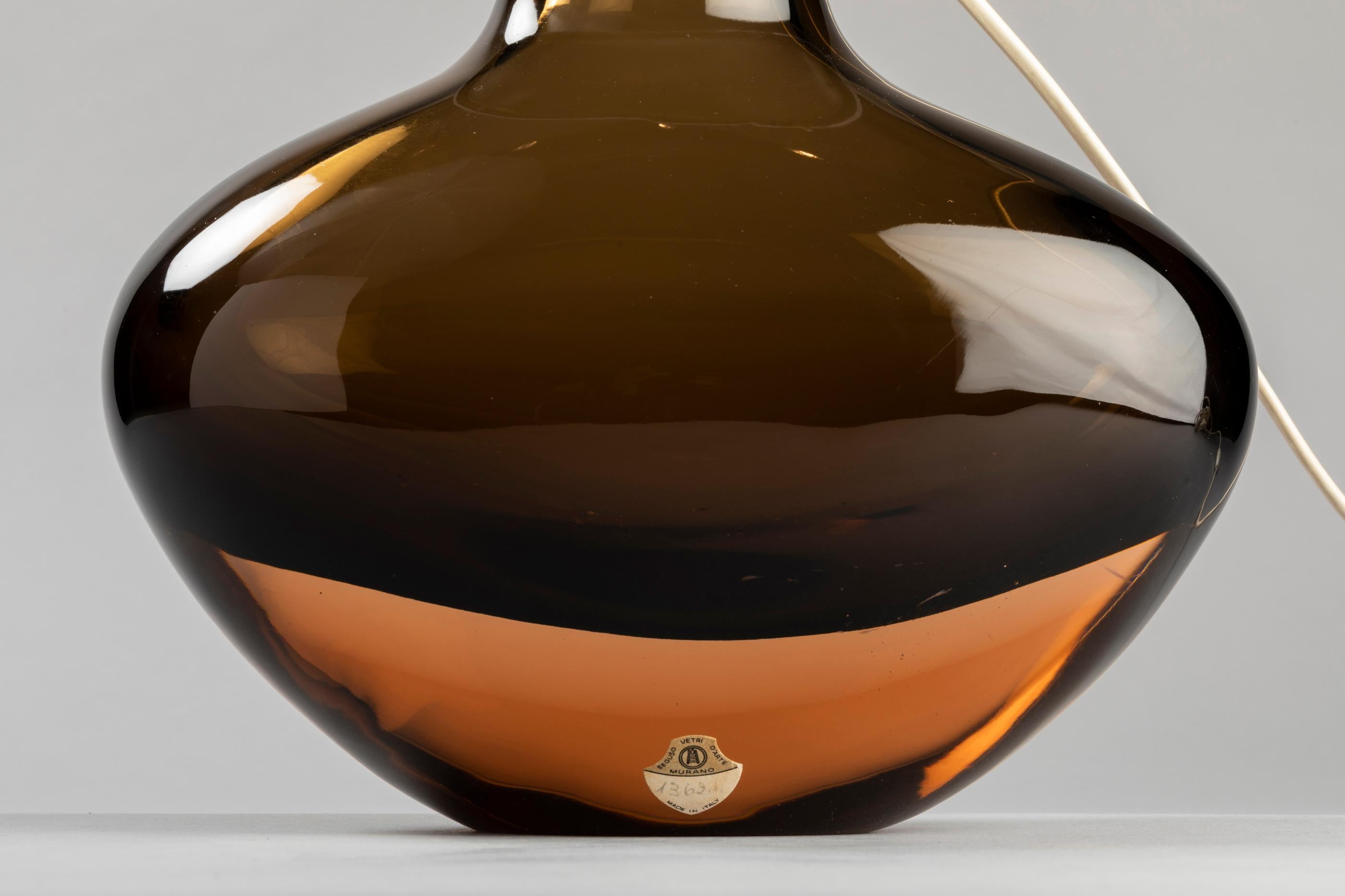 Angelo Seguso gave a new life to this vase that has been redesigned as a table lamp (for Seguso Vetri d'Arte).
A Classic Murano glass work with a brown shade for modernity. A sensual lamp with warm tones to enhance the beauty of your interior.