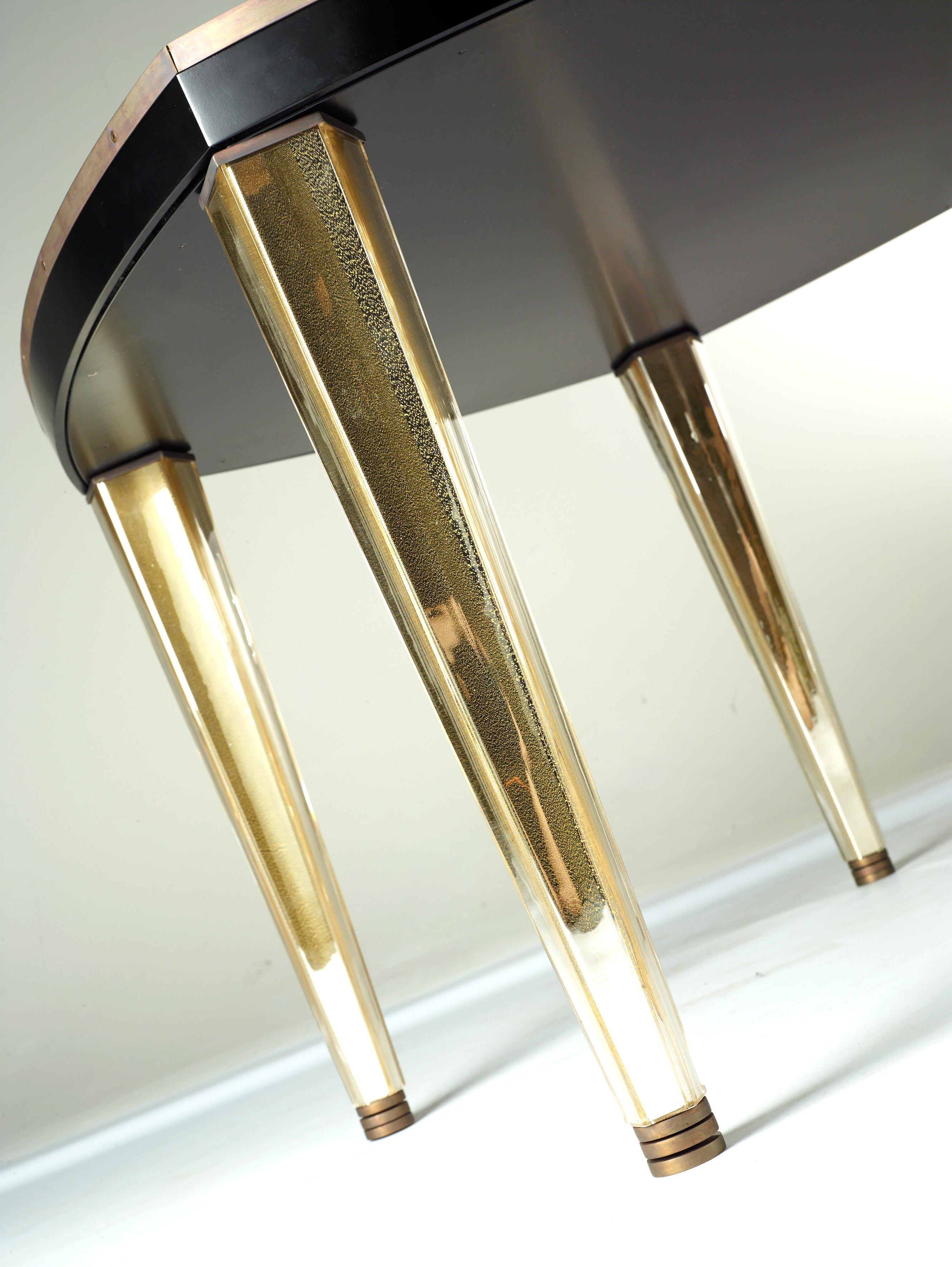 Mesa central Penta con patas de cristal de Murano de Seguso Vetri d'Arte. Un diseño elegante y versátil que puede encajar en una amplia gama de interiores. La tapa pentagonal de ébano se apoya en patas de cristal de Murano dorado. El estilo