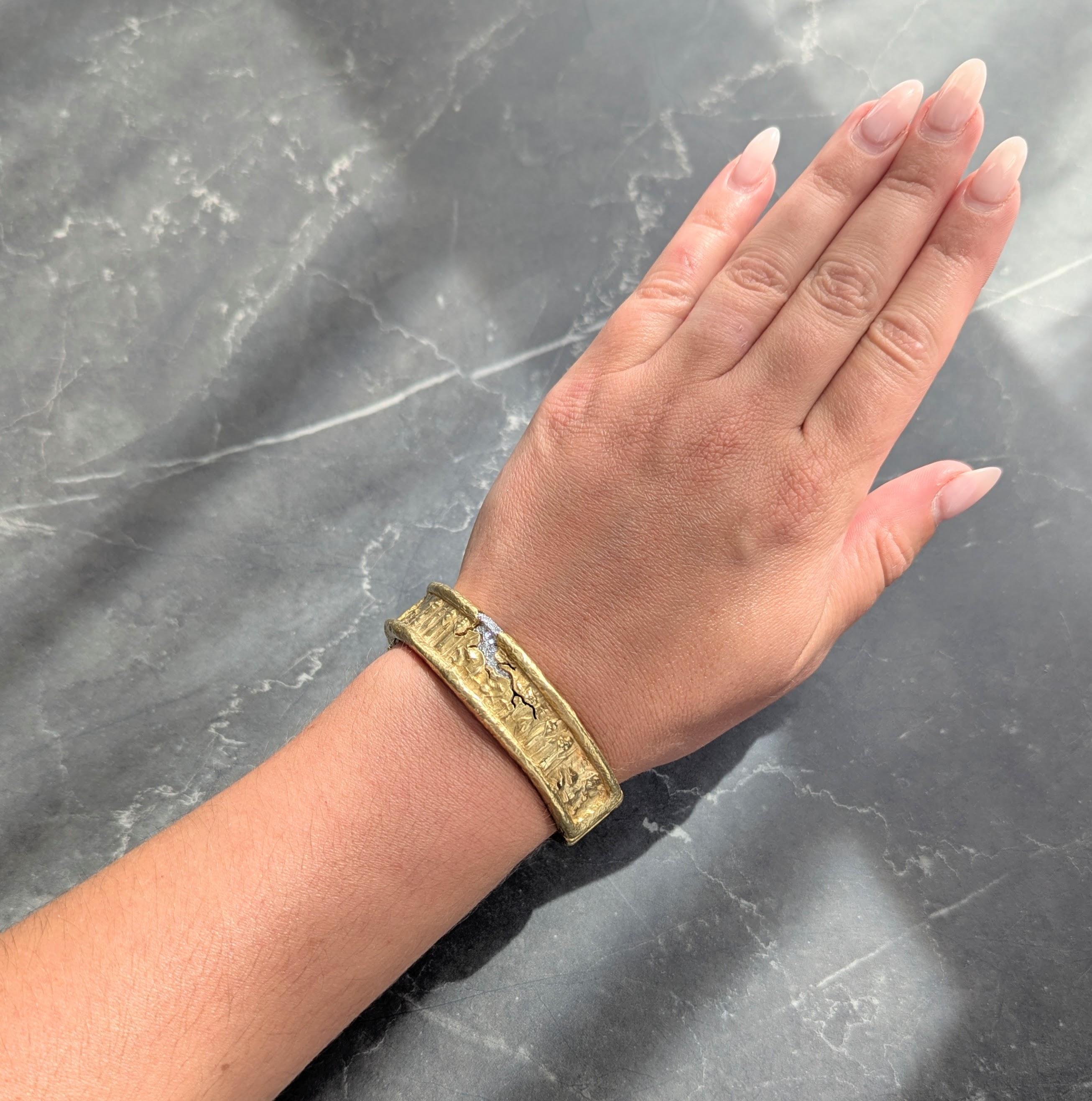 Ein breiter Armreif aus geschwungenen Gelbgoldplatten mit erhabenen, organisch strukturierten Rändern
In der Mitte tief gerillte Darstellungen von ägyptischen Hieroglyphen und Figuren
Akzentuiert durch ein Motiv aus gesprungenen Steinen mit