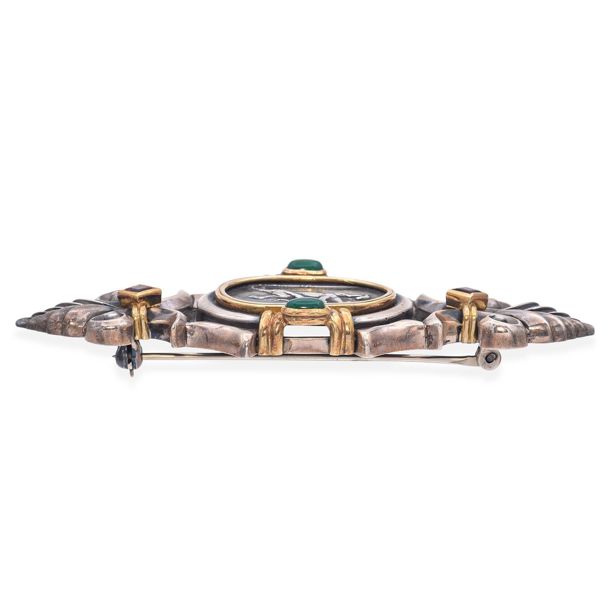 This brooch by SeidenGang showcases a central motif of Pegasus in a sterling silver medallion, framed by an ornate yellow gold bezel. Accented with cabochon-cut green Chrysoprase and square-cut orange garnets, the design is further enhanced by