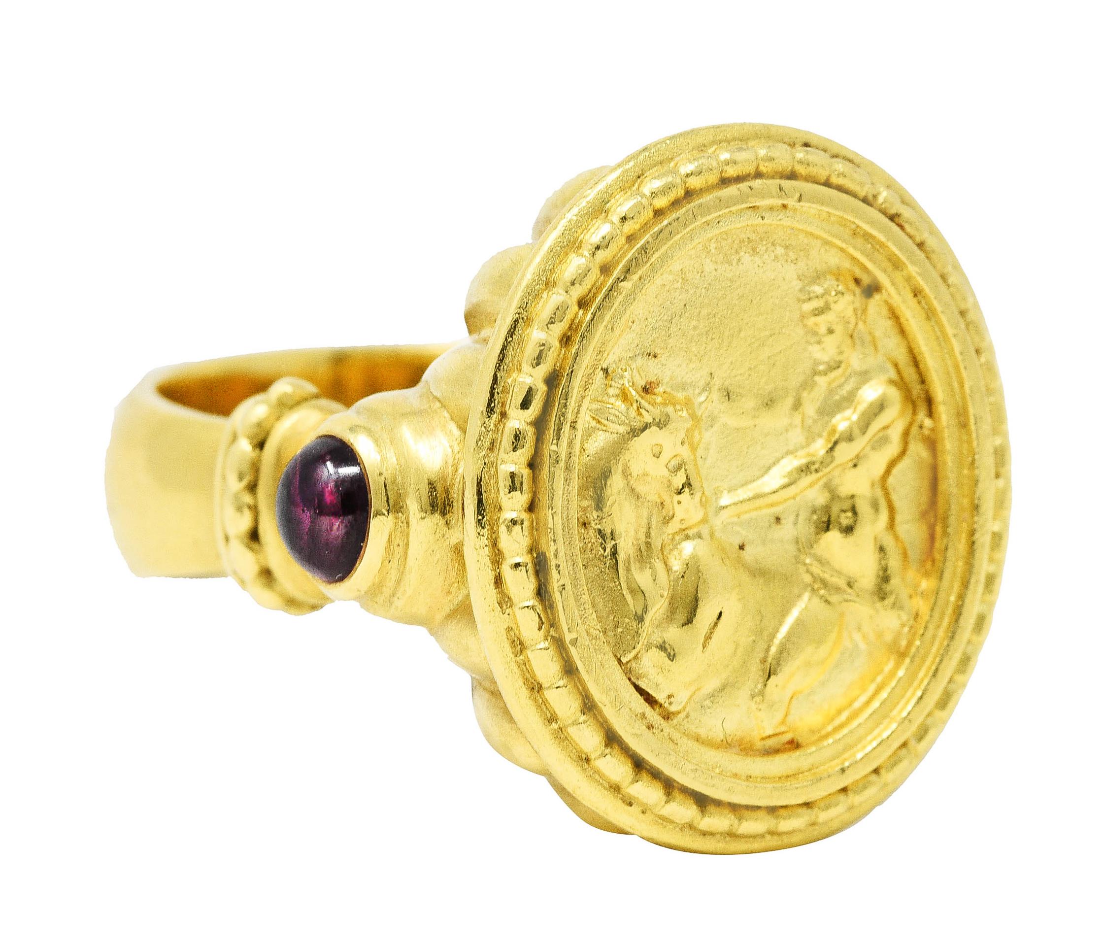 Ring centers a recessed gold cameo of the Greek hero Hercules and the Cretan bull

Accented by textured gold frame surround and deeply ridged basket

Shoulders feature 3.5 mm round bezel set garnet cabochons

Transparent purplish red in color with
