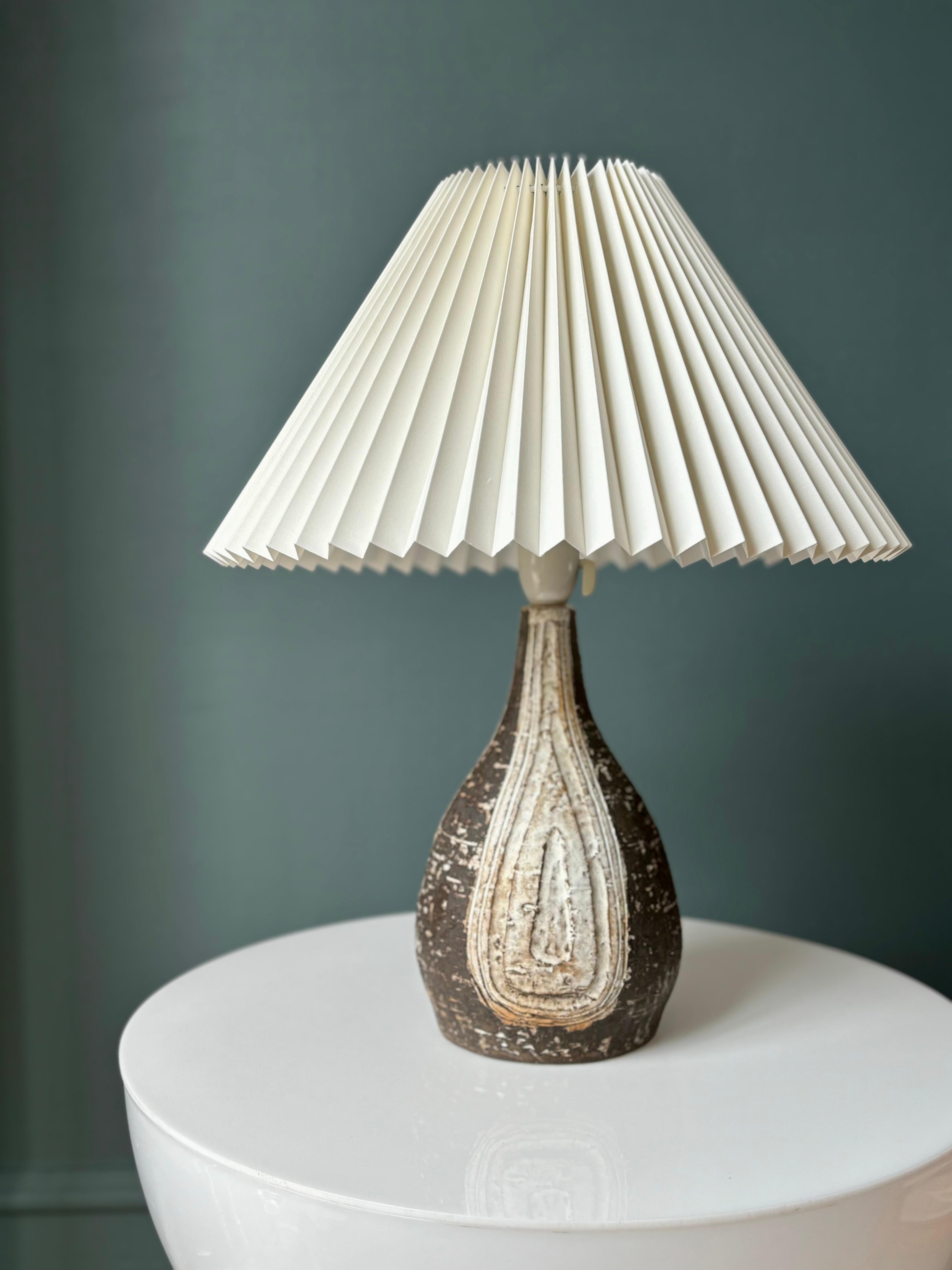 Handmade rustic brown ceramic table lamp by Danish manufacturer Sejer in the 1960s. Rustic chamotte clay with organic cream glazed relief decorations on three sides. Wired for Europe and the US. Beautiful vintage condition. 
Pleated cream linen