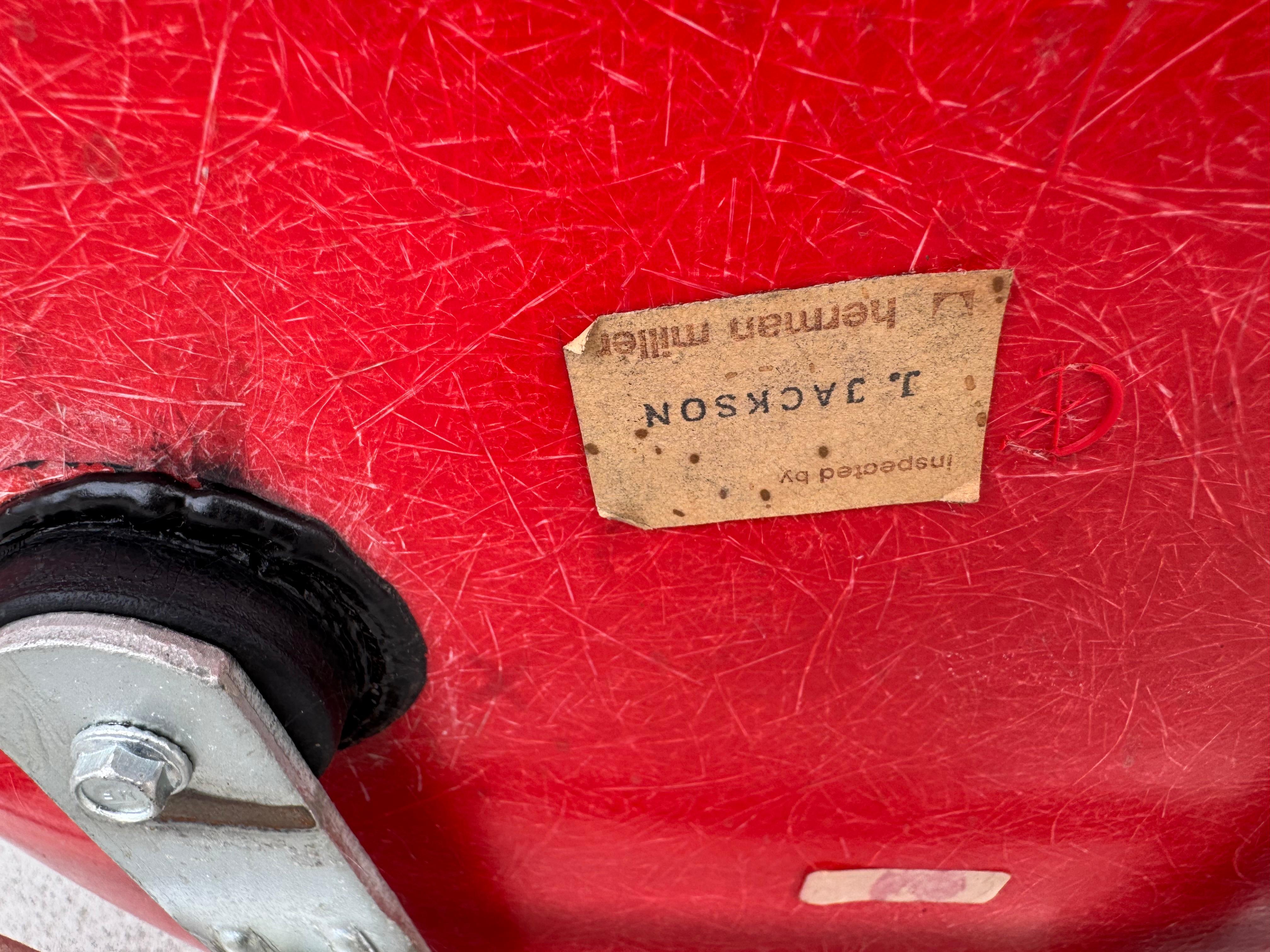 Eames für Herman Miller geformter Schreibtischstuhl aus Fiberglas. Die Tischplatte lässt sich zum leichteren Sitzen hochklappen. Behält das Label von Herman Miller. Vibrierende rote Glasfaser, schönes Gelcoat, freiliegende Fasern. Erstaunlich 