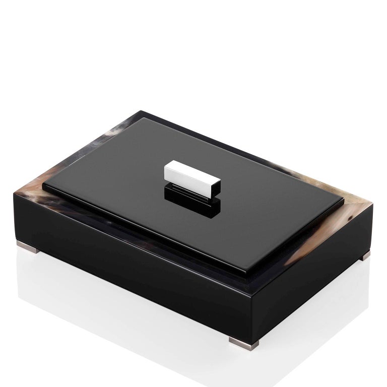 Distinguished by plush materials and essential lines, our Selene box showcases a rectangular wooden structure with a polished black lacquer finish. Enhanced by an elegant edging in Corno Italiano, this versatile box sits atop four feet in chromed