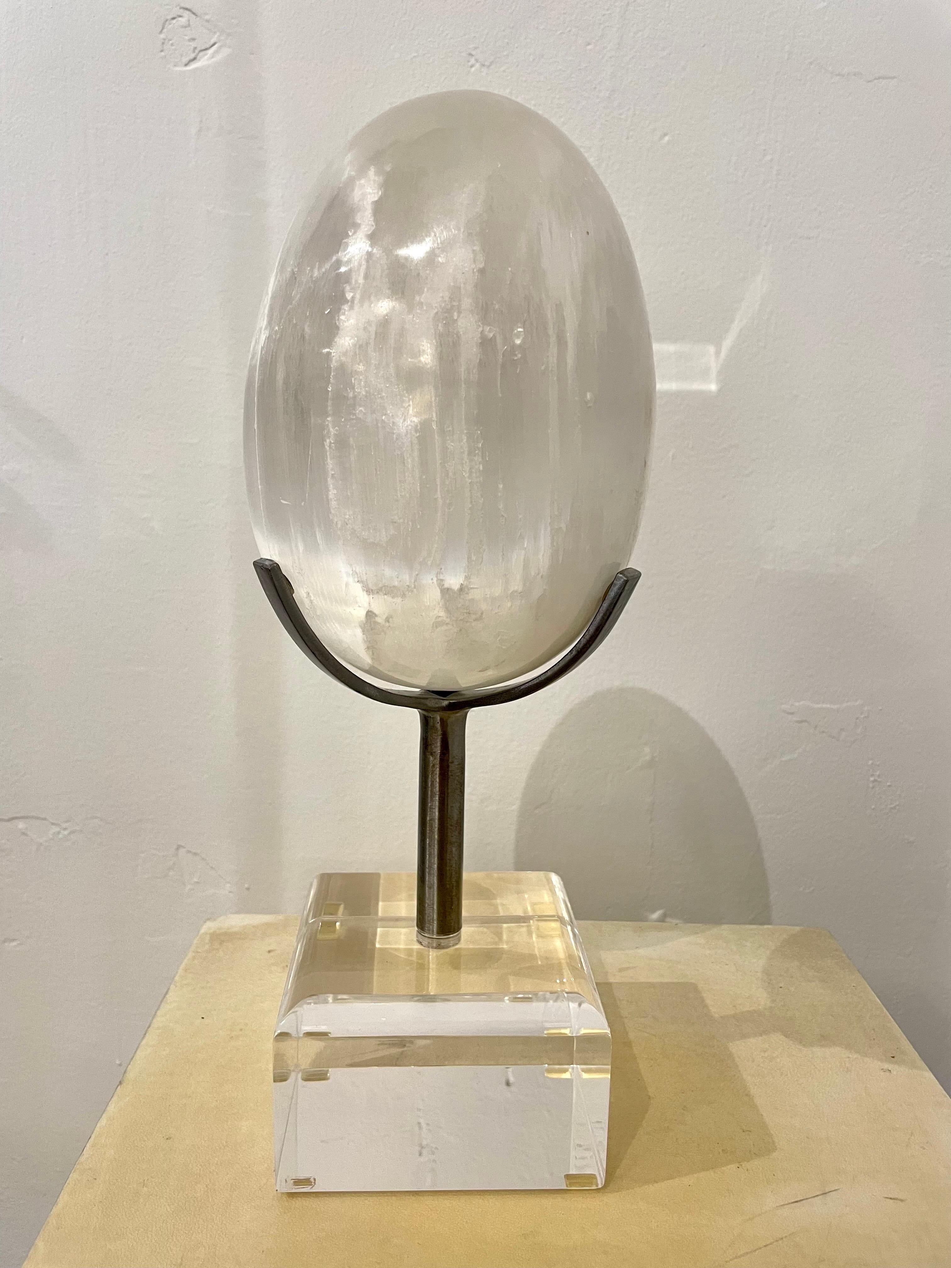 This perfectly formed crystal quartz egg shaped stone sits atop a steel arm and lucite base. Wonderful decorative piece - very organic.