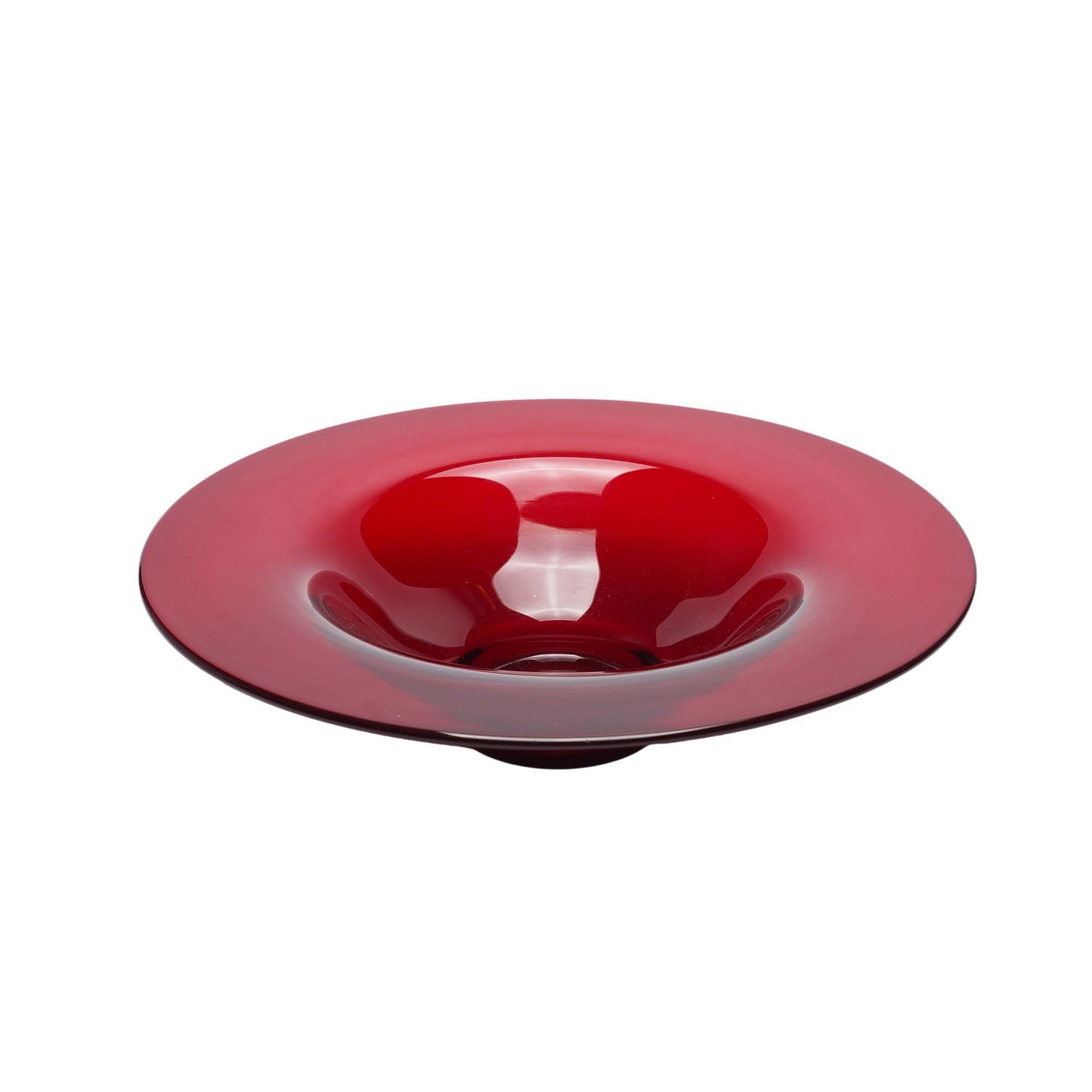 Hand blown selenium red glass footed center bowl with broad flat rim framing a shallow bowl. The foot of the bowl has the ground and polished pontil. From the early Frederick Carder period at Steuben, pre 1930. Unsigned.