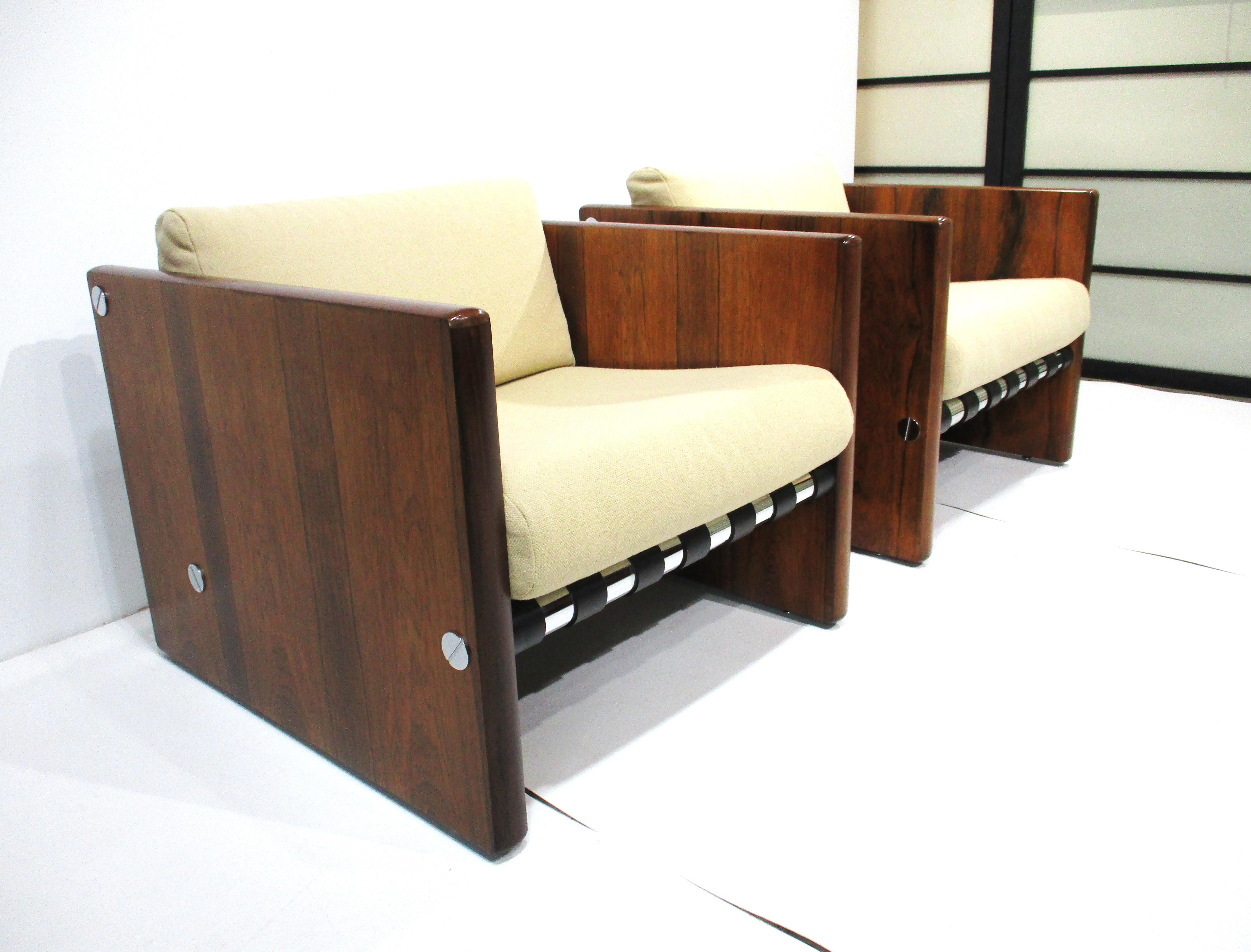 Un'eccezionale coppia di sedie da club a cubo in palissandro brasiliano con cuscini imbottiti. I cuscini sciolti poggiano su spesse cinghie di pelle nera che sono sostenute da binari in alluminio cromato con grandi viti di montaggio cromate ai lati,