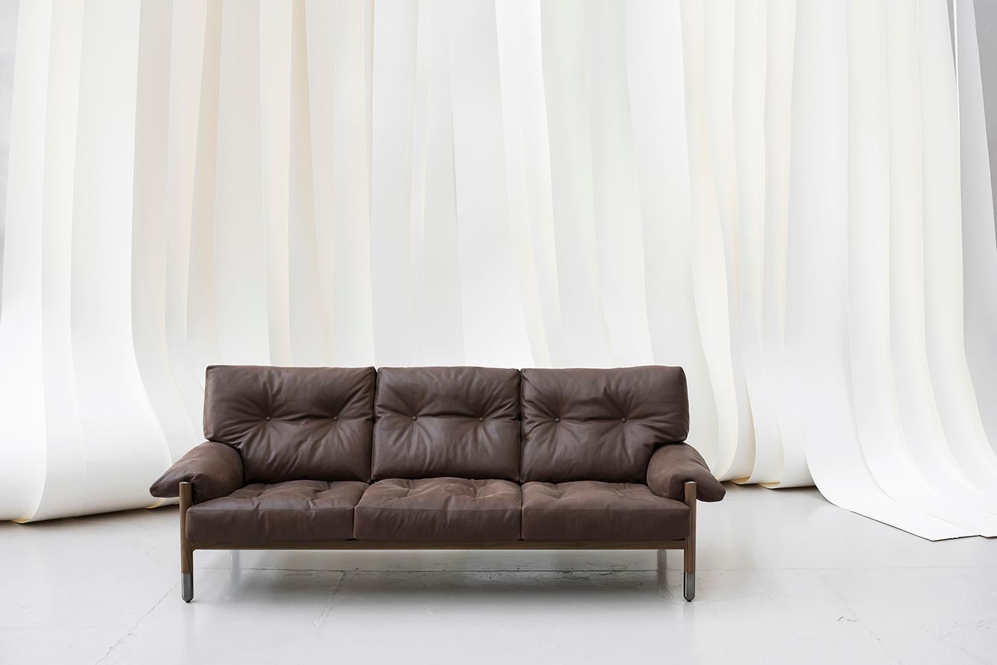 The highly elegant sofa is made using the very finest of materials: exposed walnut, elegant metal chromed details finish shiny black and belts for the support of the backrest in refined natural leather. The cushions are filled with feathers and the