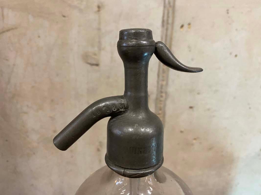Antiker Siphon aus Frankreich aus den Jahren um 1900. Die Flasche ist aus dickem, schwerem Klarglas gefertigt und hat einen Verschluss aus Zinn. In der Kappe ist das Wort UINETTE und die Zahlenfolge 10165 eingeprägt. In den Glaskörper ist auf der