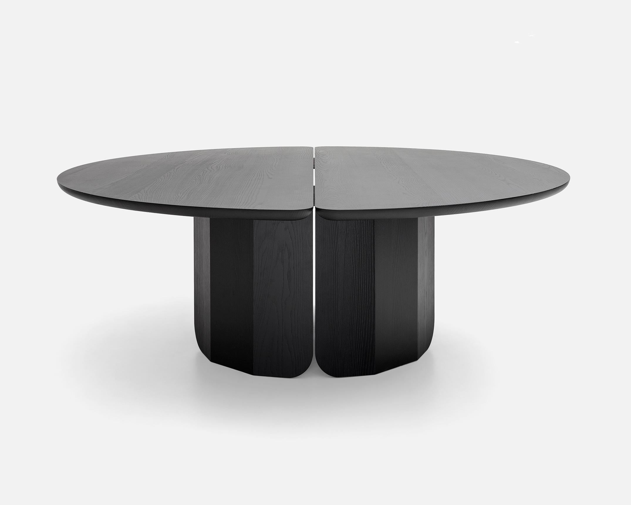 The table has a circular top in black-stained brushed ash, that can have a matt or glossy finish. It is composed of two semi-circles the form a central slit: the edge is rounded and curves inwards towards the center, highlighting the juxtaposition