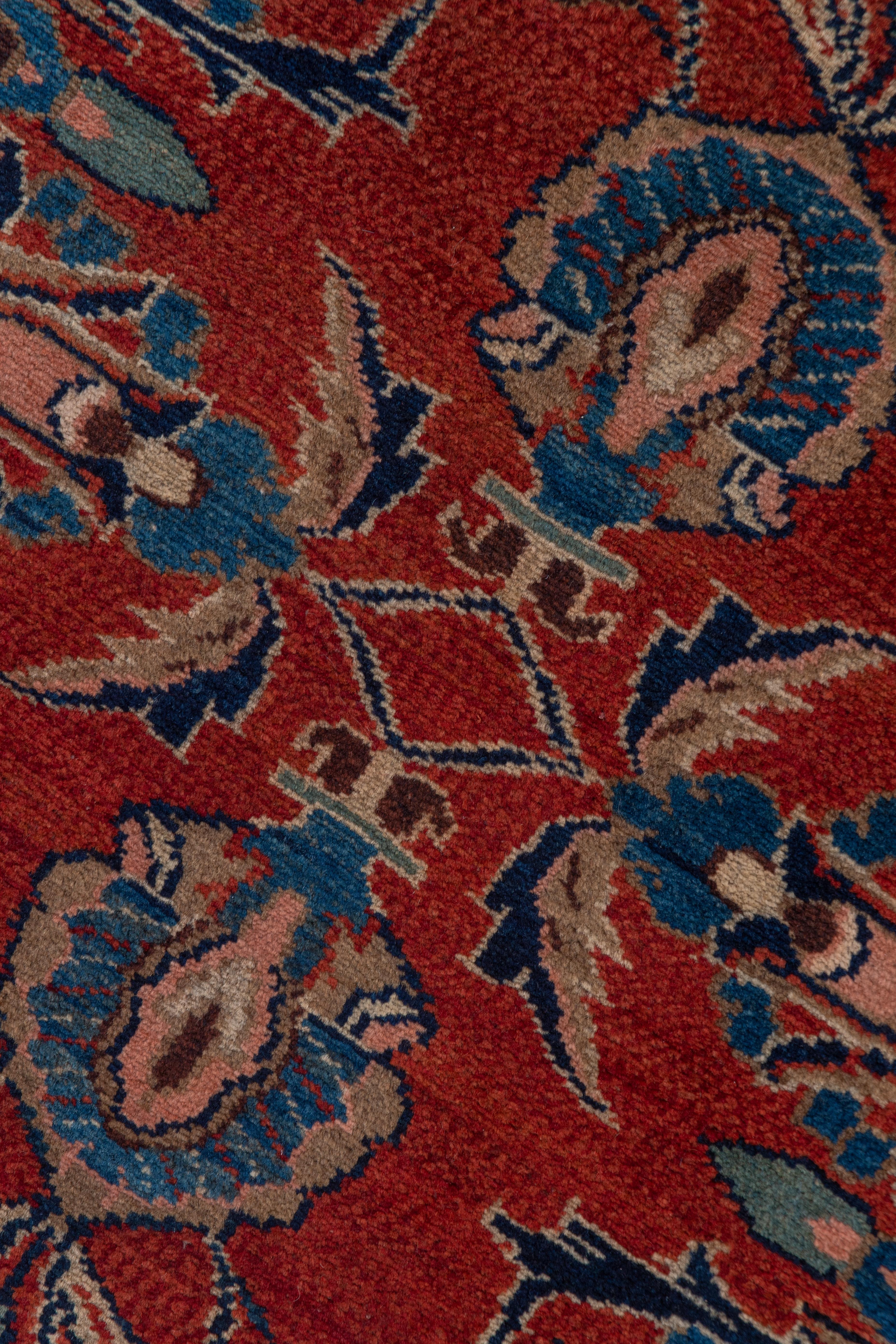 This semi-antique Hamadan area village runner features a cranberry scarlet field supporting a palmette and angular vine segment design in one column, detailed in navy, royal blue, ivory, green and pink. The dark blue narrow main border shows a