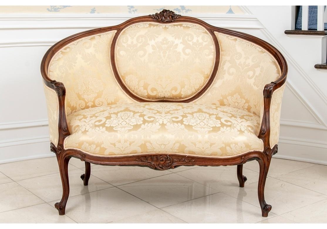 A classic French High Back Settee with a finely carved frame with a center back oval and carved leafy crest. The arms with leafy scrolled ends, the shaped seat rail with carved leafy cartouche, and the cabriole legs with scrolled feet. Upholstered