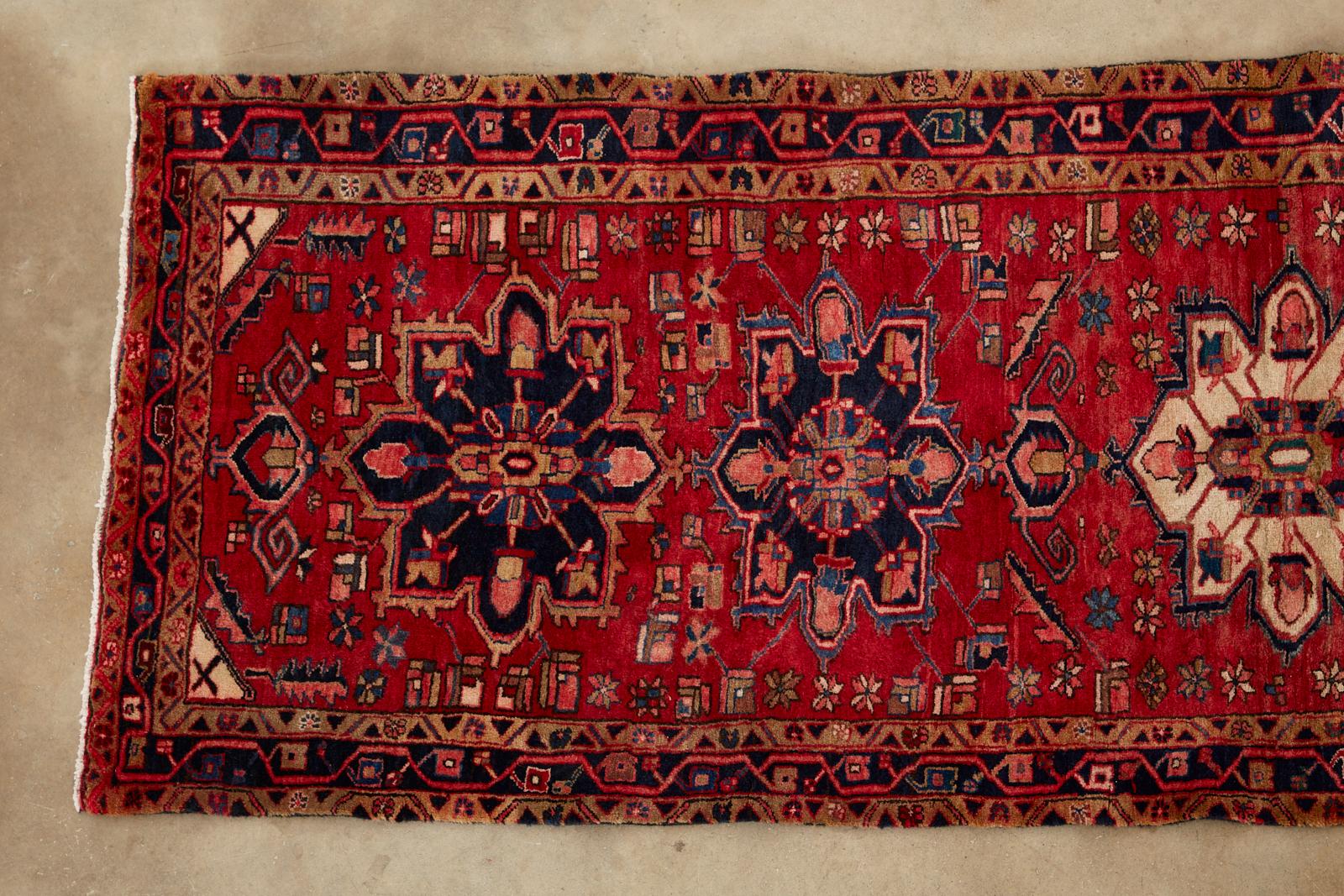 Midcentury semi antique Persian Heriz runner rug featuring a tribal design style. The carpet has five stacked medallions centered by a cream colored medallion. Gorgeous reds and pinks run throughout the field and border with colored symbols. The