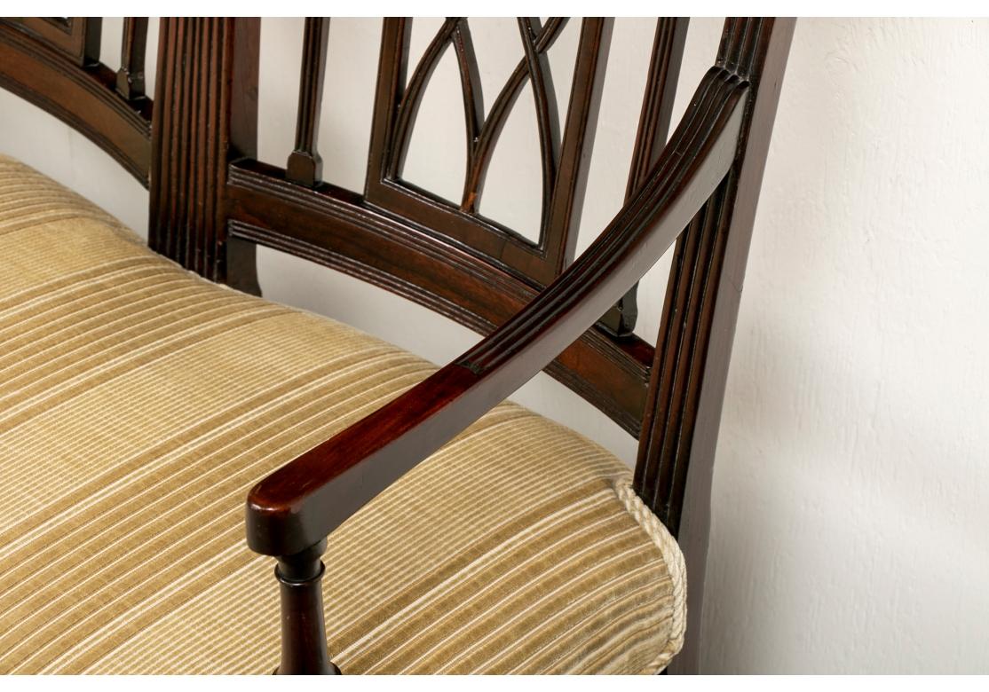 A three seat settee with curved back sections. Each with fluted supports and arms. The backs with carved lotus flowers flanking open X supports. The arms with turned supports. Raised on ribbed cylindrical tapering front legs with peg feet and