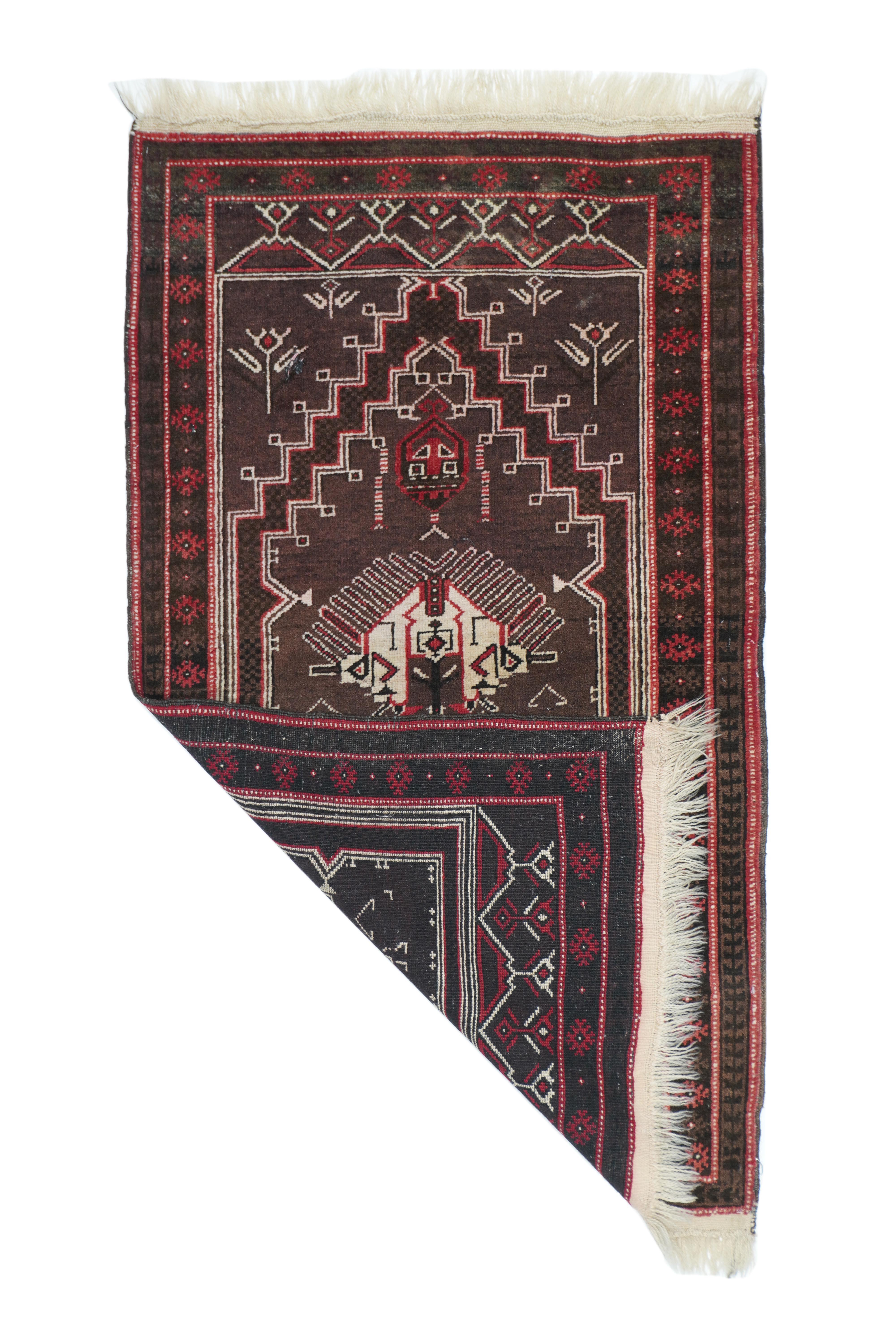 Creatively interpreting a central Turkish style with a stepped wine red floating niche, on a dark blue stepped field, with flowering spandrels and a floral panel at each field end. Two large finger-fringed palmettes in the field are the most salient