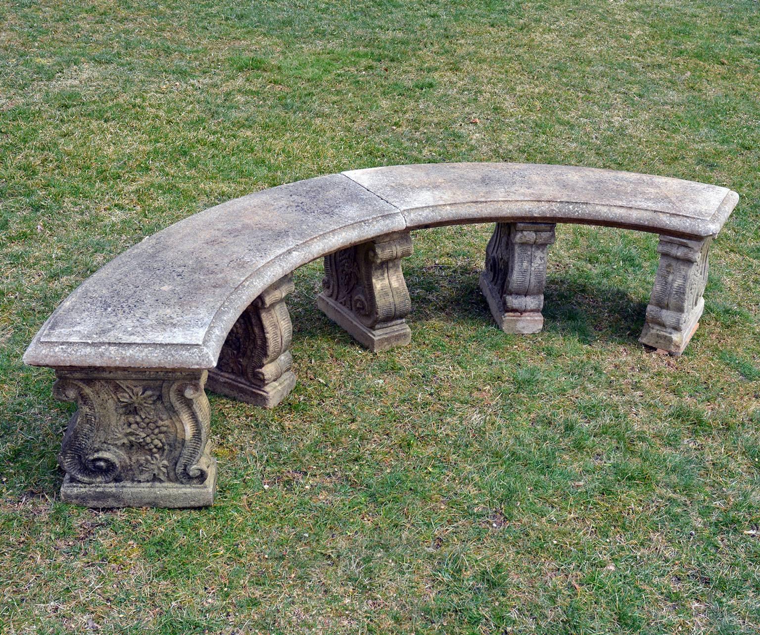 A quarter-circular composition stone bench, the slab top in two parts, the five supports with scrolled volutes and botanical motifs, English, circa 1980. Measures: 18 ins. high, 88 ins. overall width, 32 ins. overall depth.