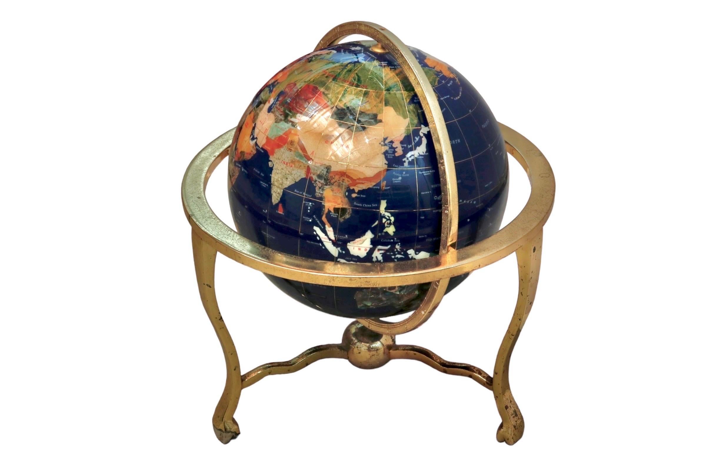 A desk top globe decorated with oceans of lapis and continents made with semi-precious gemstones. A brass meridian encircles the globe and is attached at the north and south poles, as well as to the brass base at each side, allowing the globe to be