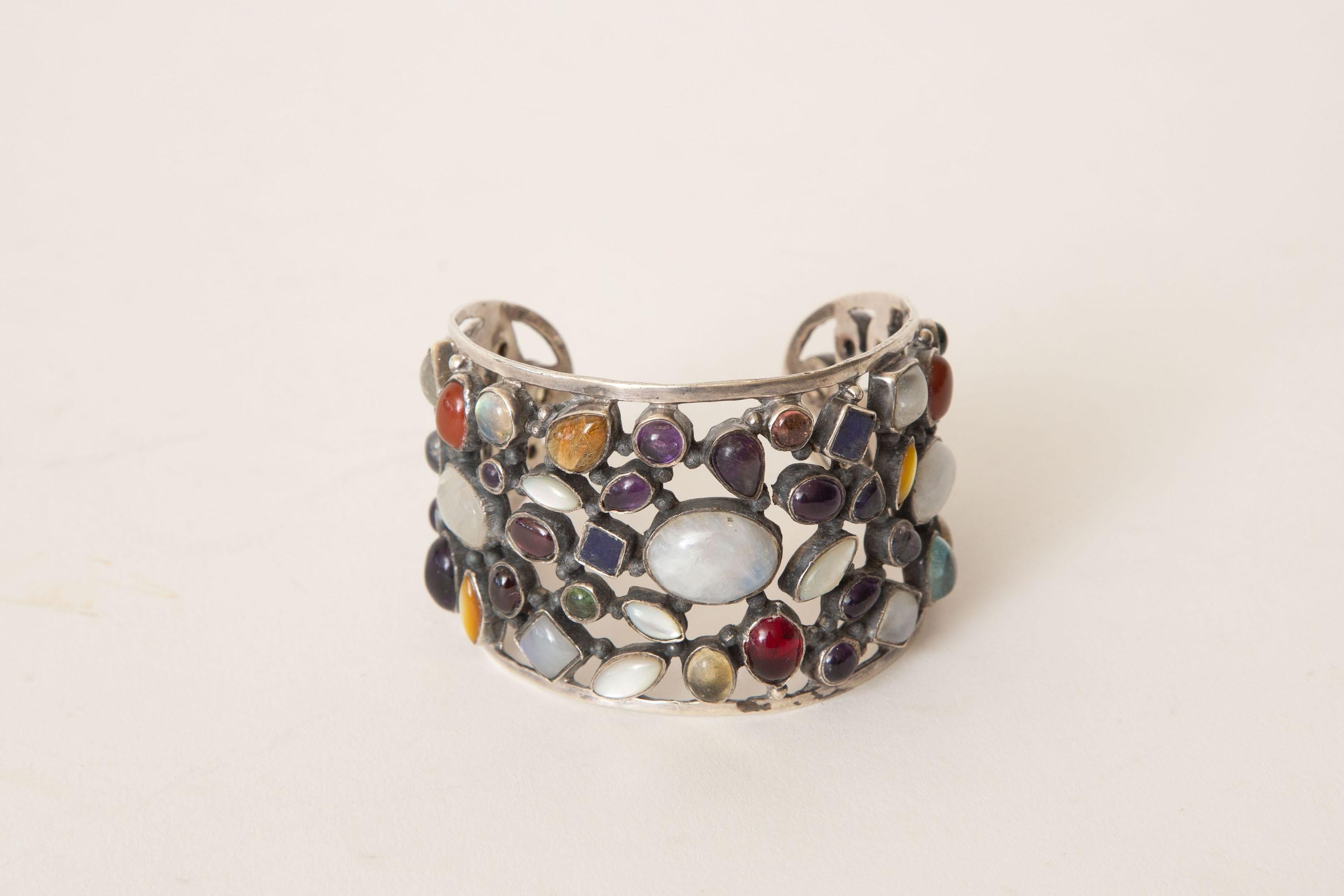 Ce superbe bracelet manchette, entièrement travaillé à la main, est une magnifique combinaison de pierres semi-précieuses de différentes formes et couleurs, serties sur un filigrane d'argent sterling. L'opale, le grenat et l'améthyste ne sont que