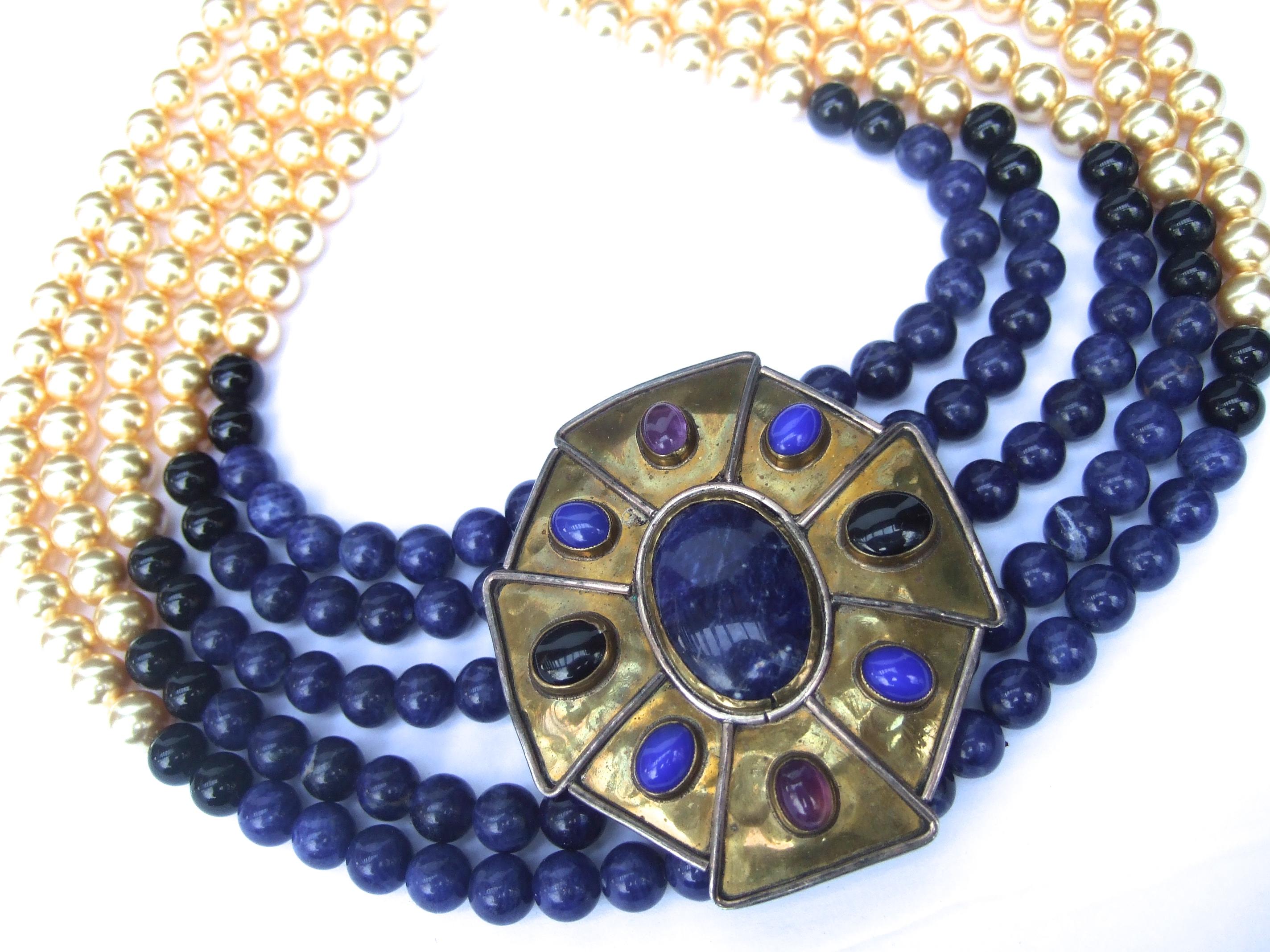 Semi precious lapis, amethyst, jet onyx glass enamel suntan pearl choker necklace c 1970s
The dramatic necklace is designed with a large stationary brass pendant 
in the center

The brass pendant is embellished with semiprecious lapis, amethyst, 