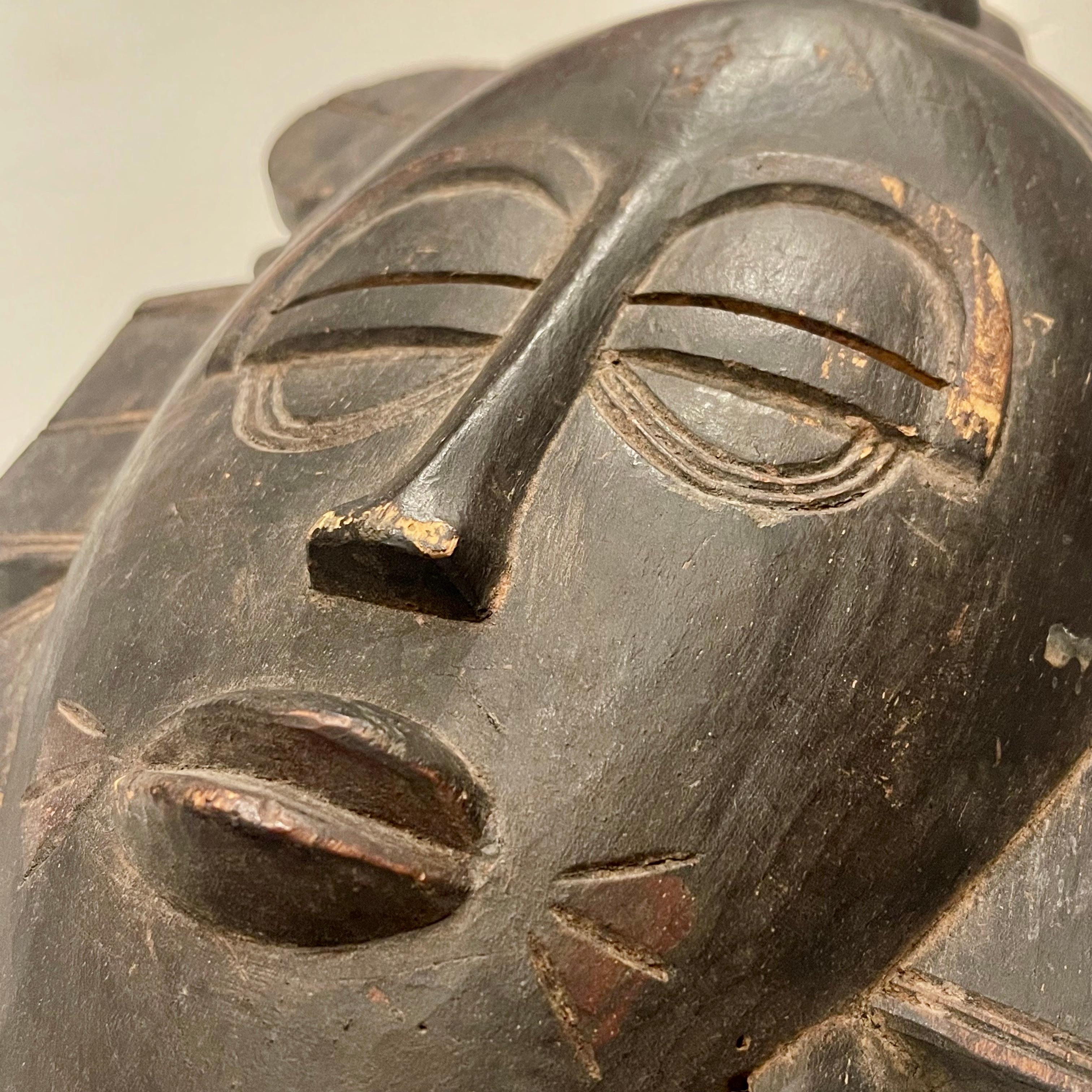 A strikingly darkly patinated and geometrically inscribed ritual mask made by the Senoufo people of the Ivory Coast. This delicately carved mask, with its characteristic arched eyebrows, oval head and narrow eyes represents a beauteous female