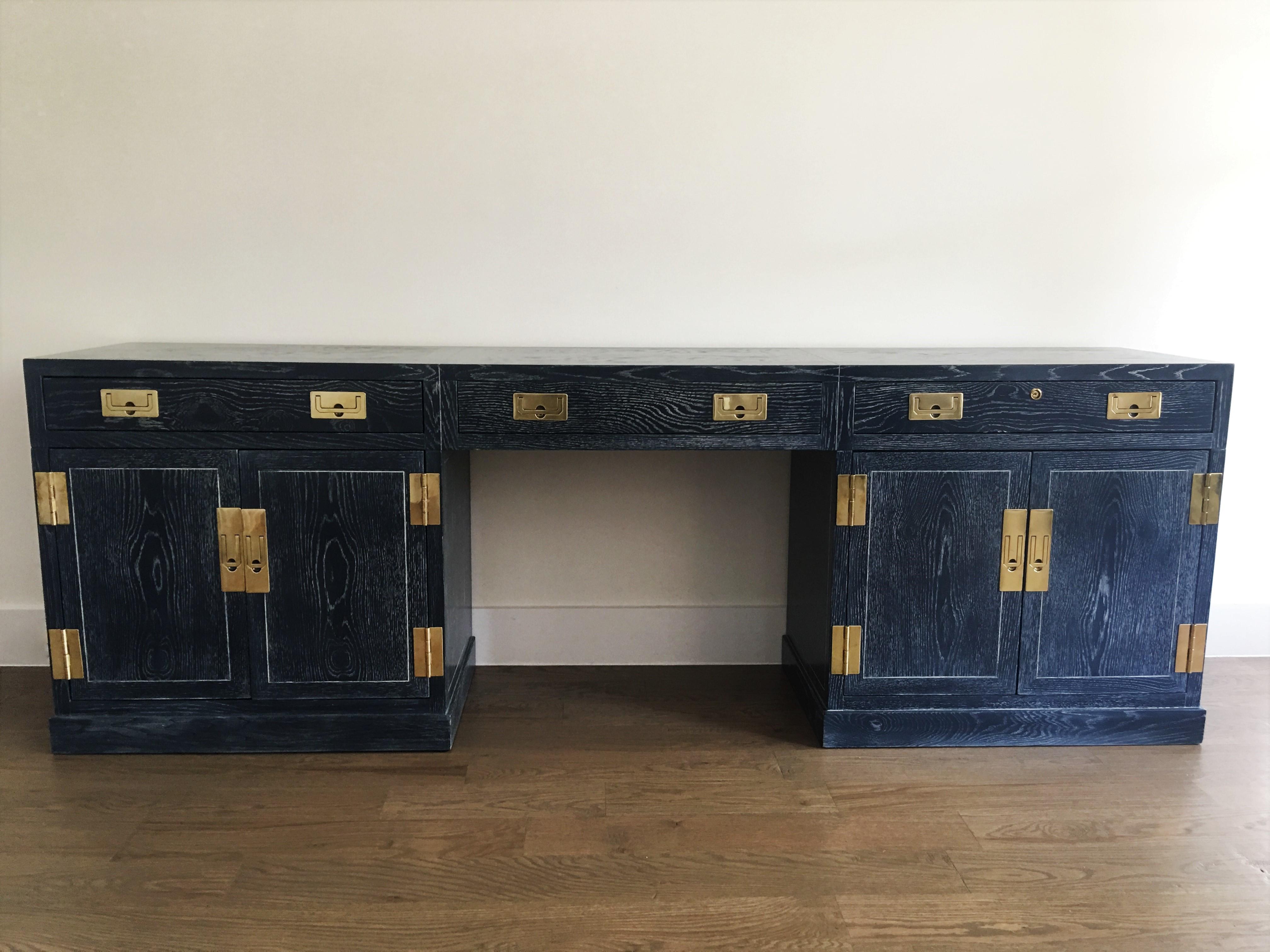 A vintage Campaign style cerused oak and brass credenza or desk by Henredon has been newly refinished. This rectangular top desk features a kneehole drawer flanked by a drawer over two cabinet doors to each side. The drawers and cabinet doors
