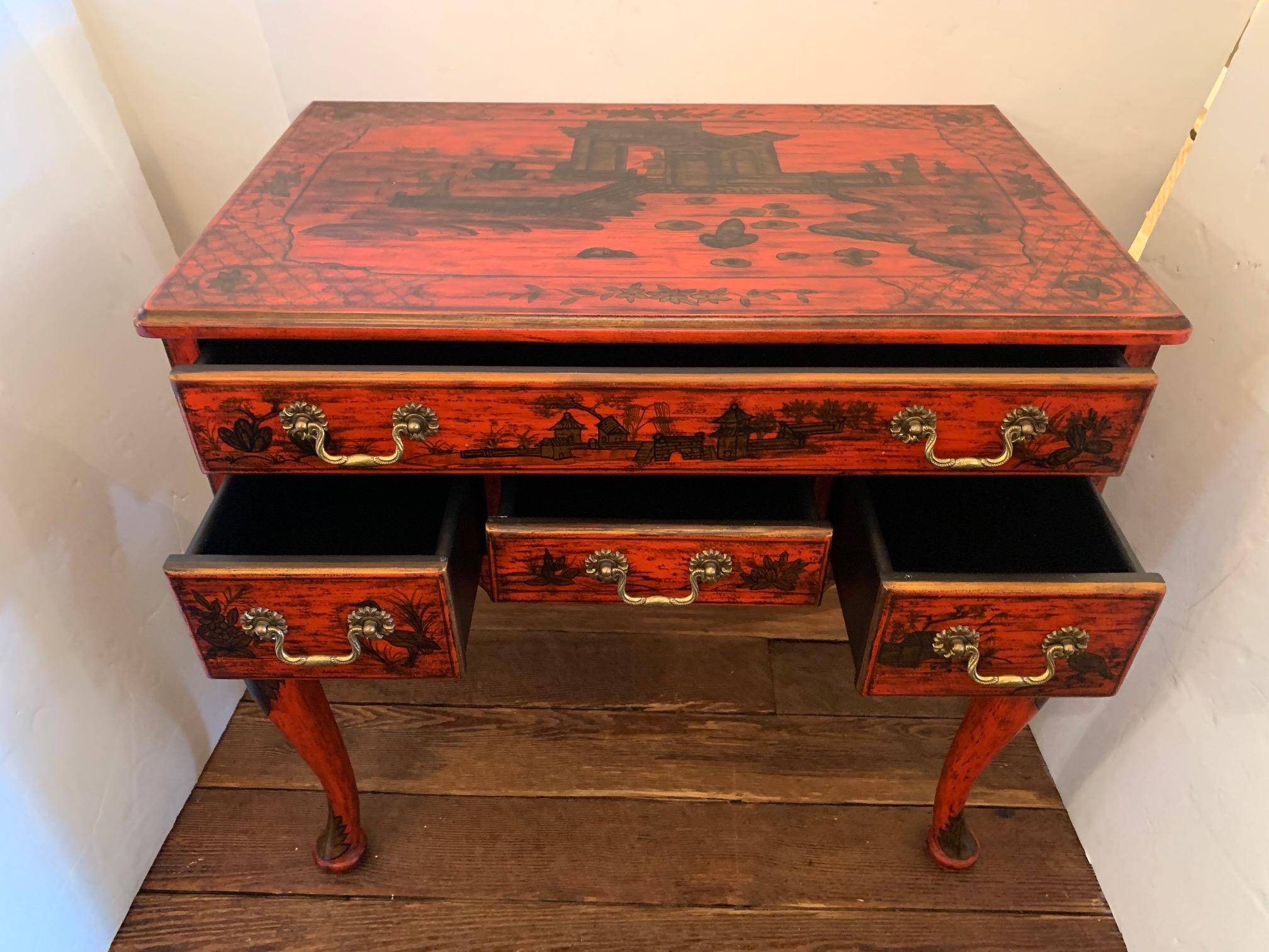 Chic tomato red, gold and black chinoiserie style console with drawers, having gorgeous antiqued finish and lovely pagodas, flowers and hatch work decoration. There is one long drawer over 3 smaller drawers with classic brass hardware and cabriole