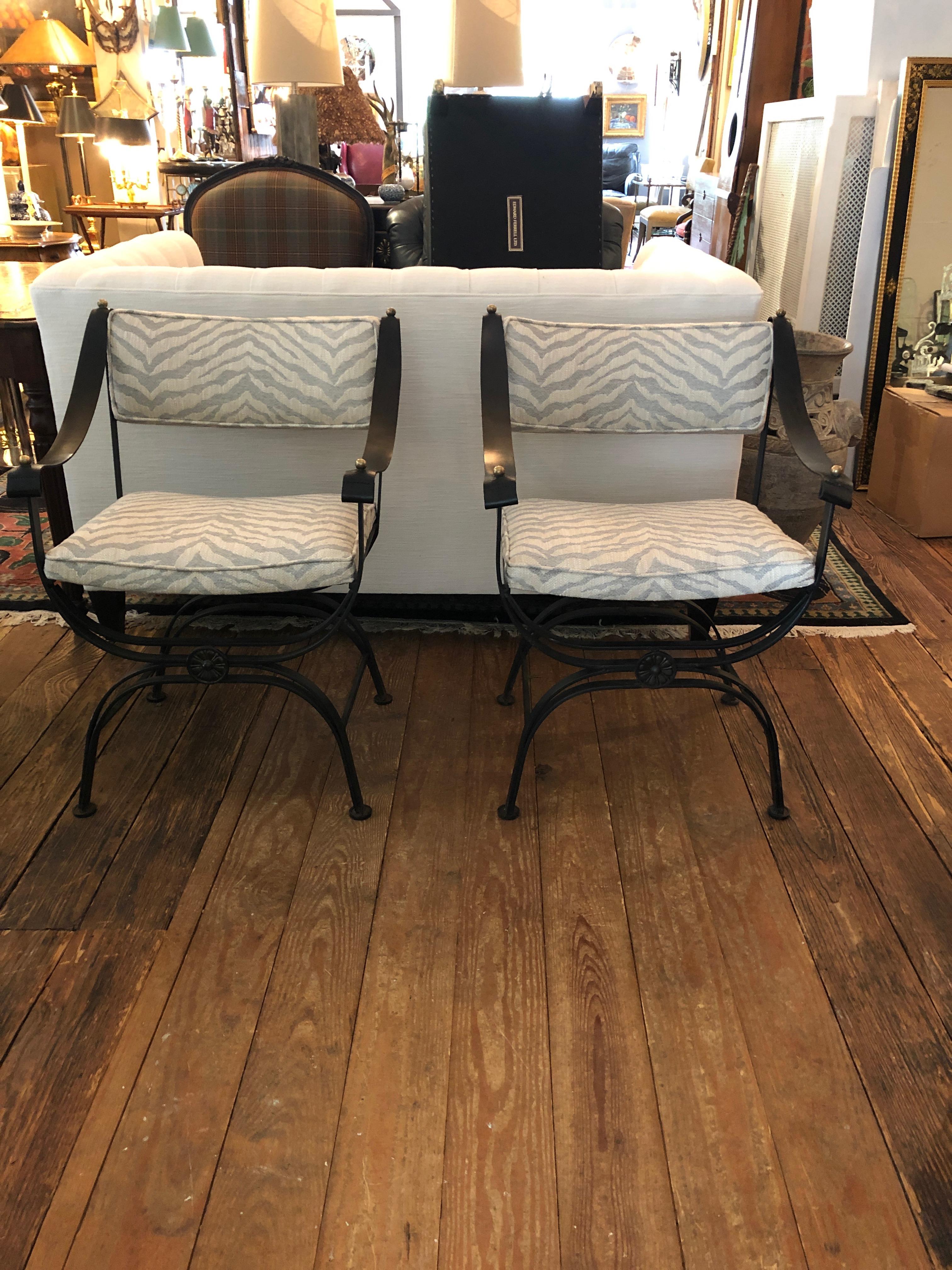 Fabulously stylish Campaign style vintage club chairs having airy yet heavy wrought iron frames and supple leather strap arms accented with brass knobs. New upholstery is neutral contemporary animal print. Comfy, substantial and the coolest chairs