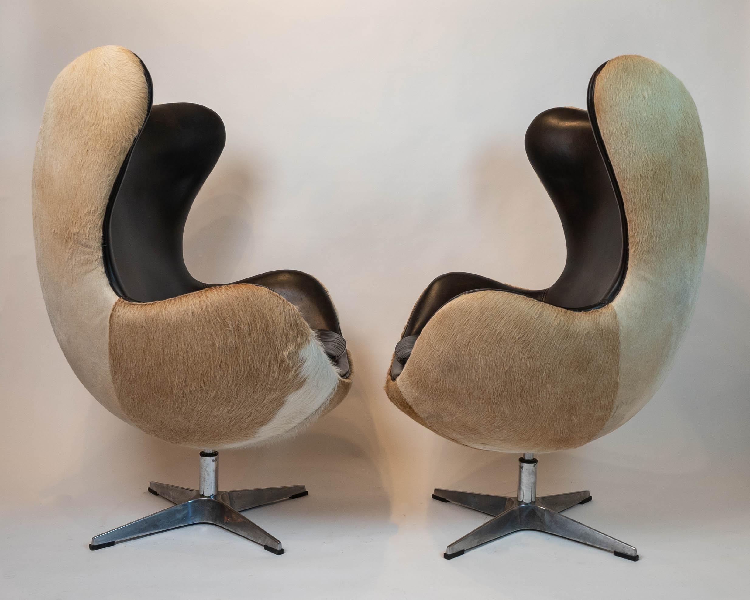 Show stopper iconic pair of vintage limited edition reproduction Arne Jacobsen Copenhagen inspired egg chairs having fiberglass shells upholstered with a sandy toned hair on hide on the exterior and contrasting supple black leather on the interior.