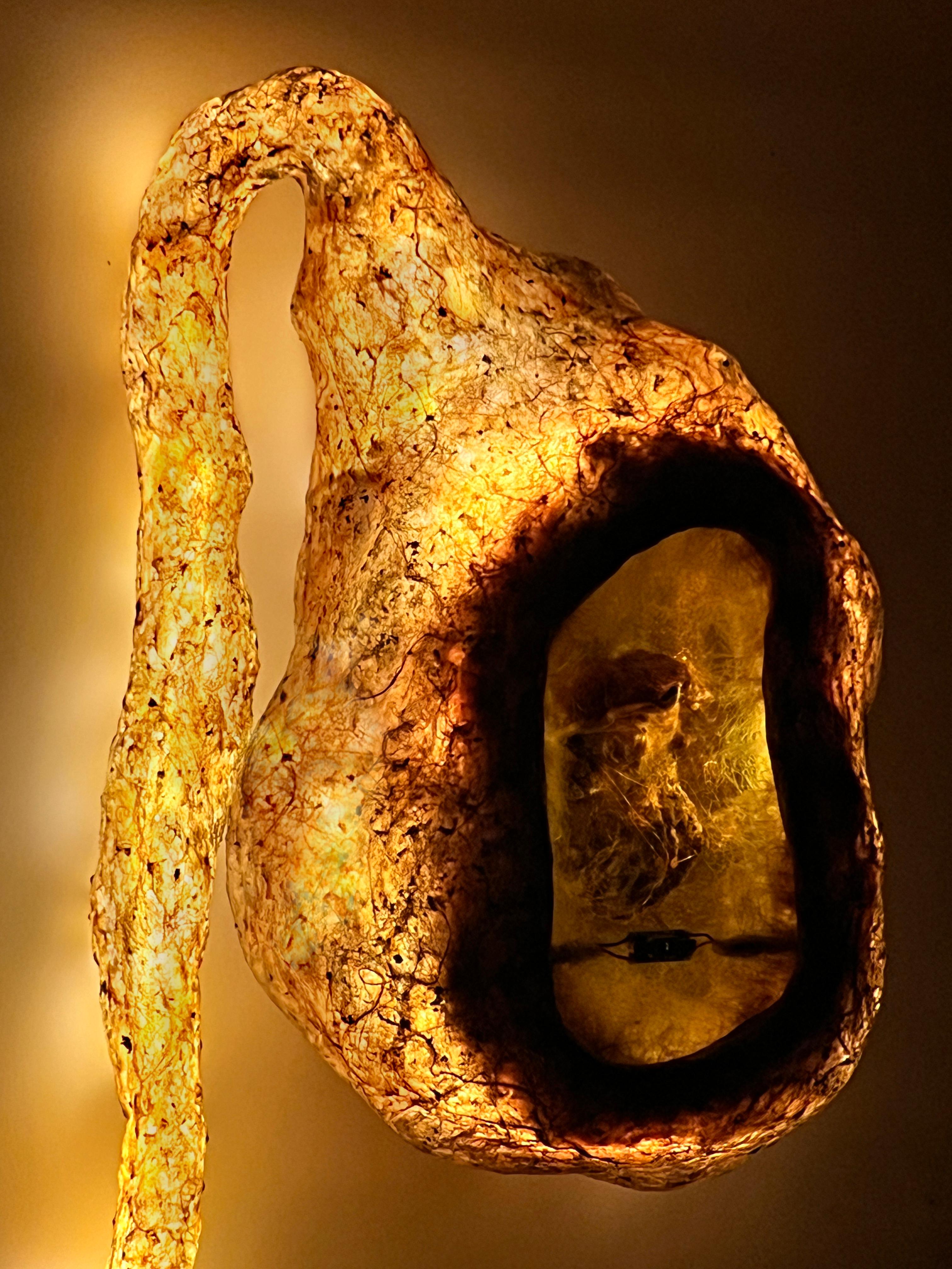 MATERIALI: BIOPLASTICA DELL'ARTISTA A BASE DI ALGHE E COLLAGENE RESISTENTE ALL'ACQUA, SENSORE DI MOVIMENTO, SPECCHIO DI SORVEGLIANZA DORATO, STRISCE LUMINOSE A LED, FIBRE DI CANAPA, COLORANTI NATURALI AL MIRTILLO, ALLA TUMERICA E AL BEEROOT, FUNGHI