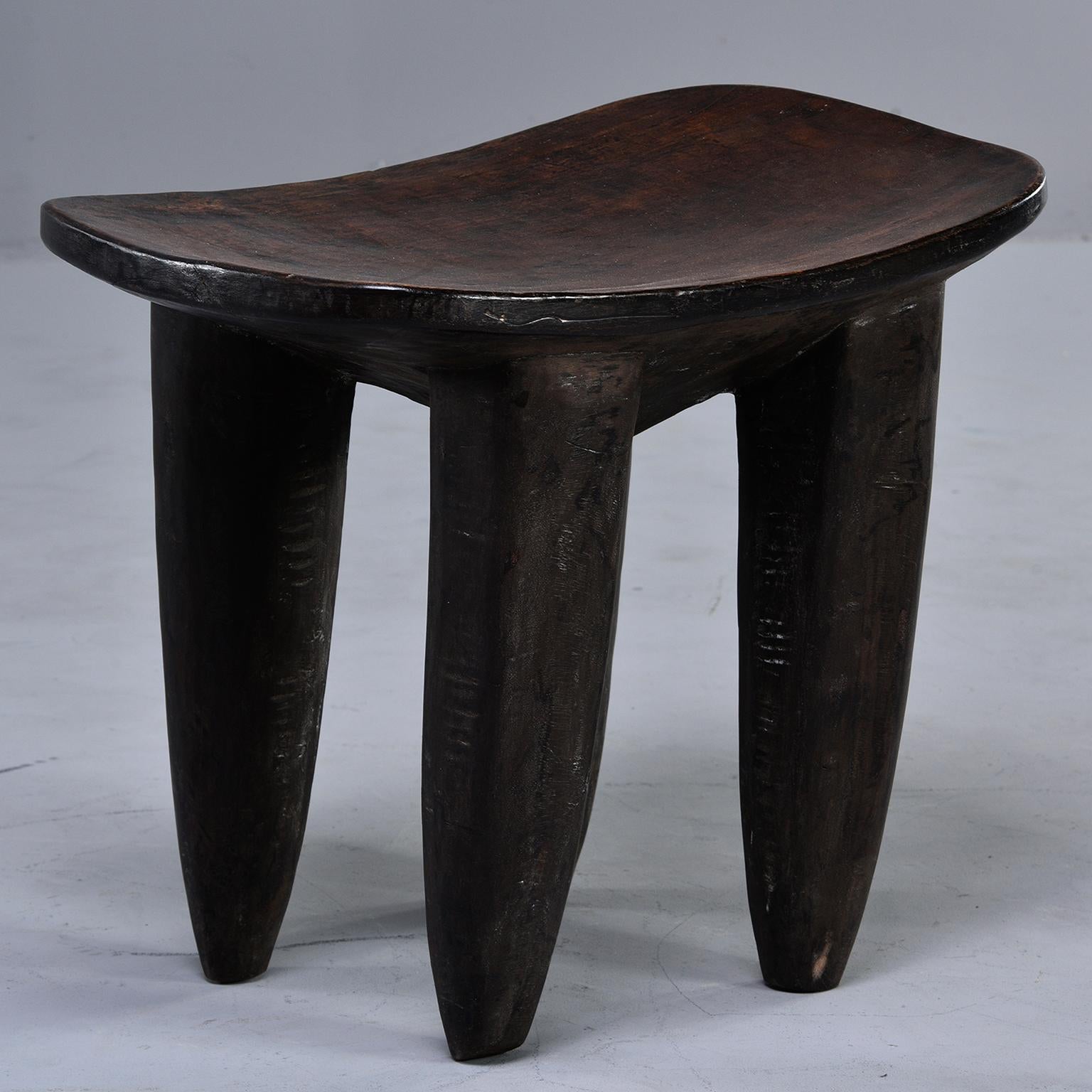 Senufo hand carved stool or side table features dark stained wood with a slightly curved top and thick, tapered legs, circa 1980s. The Senufo people are from Africa’s Ivory Coast.