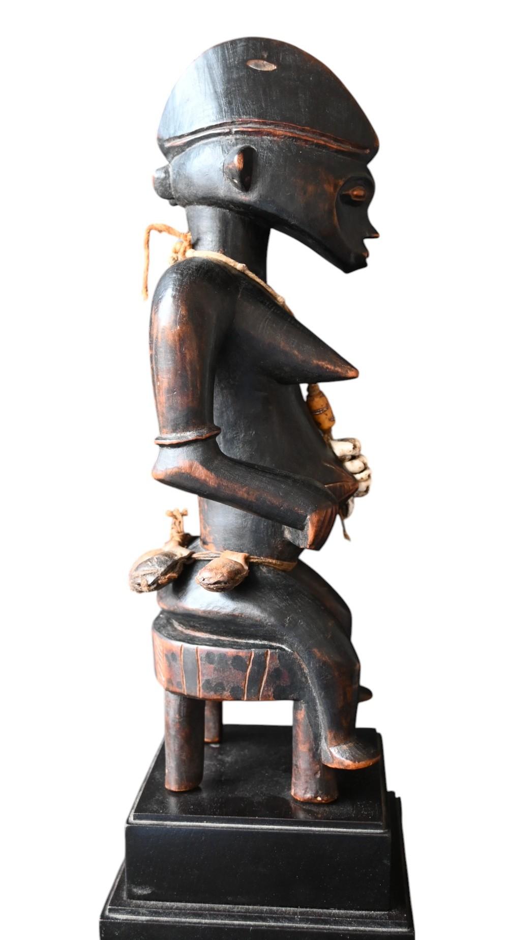 Senufo Seated Female Figure – Early 20th Century
Region: Northern Ivory Coast / Burkina Faso / Mali
Culture: Senufo
Medium: Wood, organic fibers, cowrie shells, pigment
Height: 33 cm (39 cm incl. base)
Provenance:

Jean-Pierre Laprugne / Galerie