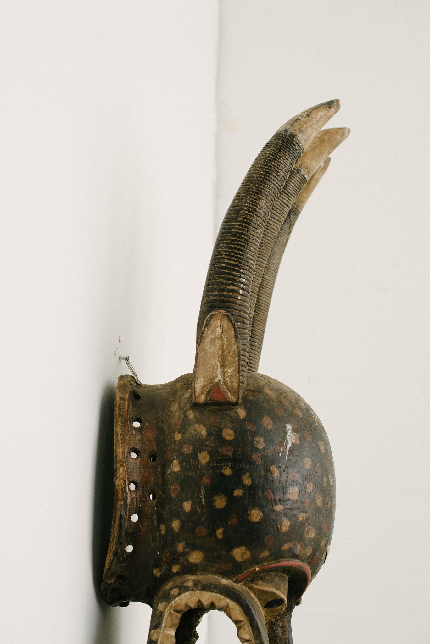 A 20th century carved and painted Senufo style mythical beast African mask. This decorative mask is whimsically painted with a spotted face, having three horns and a gaping mouth with carved teeth.