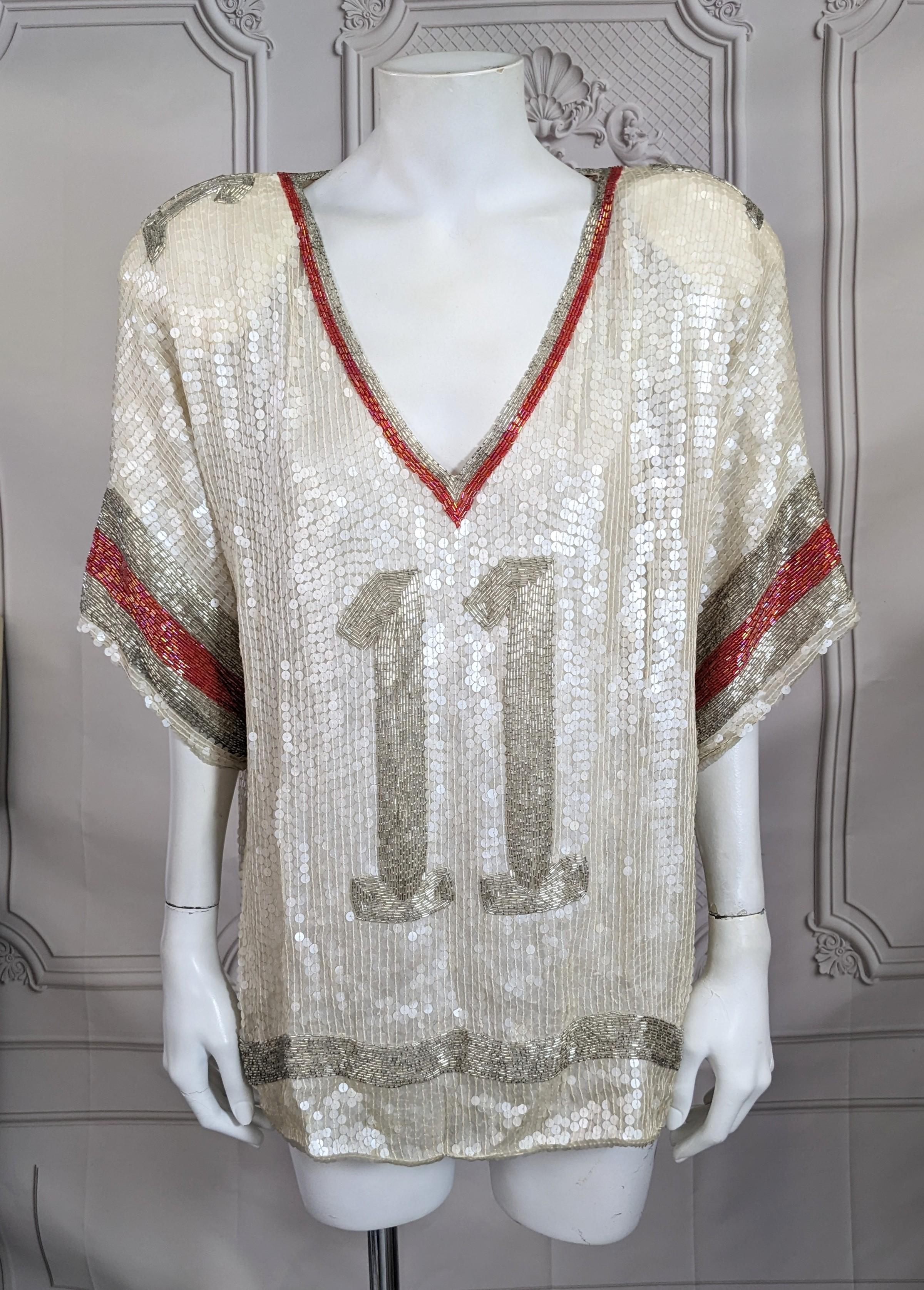 Maillot de football à paillettes des années 1980. Paillettes de nacre mates avec des accents de perles argentées et rouges irisées. Coupe ample et facile avec de larges pad aux épaules. Le 