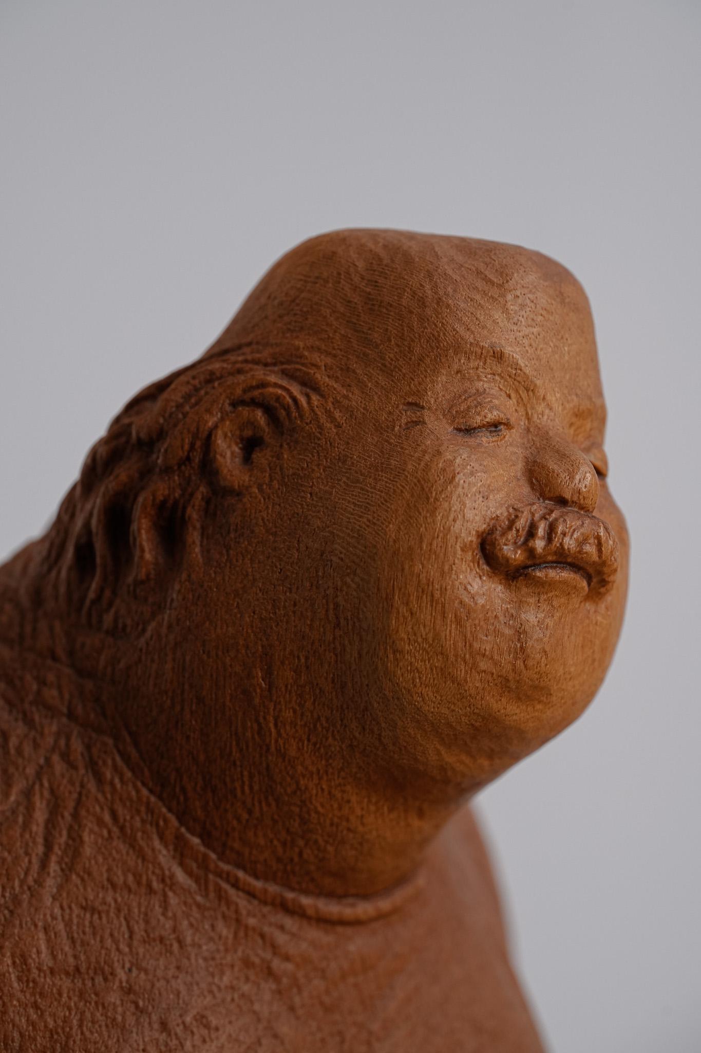 An Afternoon Break ist eine Holzskulptur voller Leichtigkeit und sanftem Humor. Ser Uang Huang zeigt einen Vorstandsvorsitzenden, der inmitten seines hektischen Lebens bei einem ruhigen Nachmittags-Haarschnitt einen seltenen Moment der Ruhe findet.