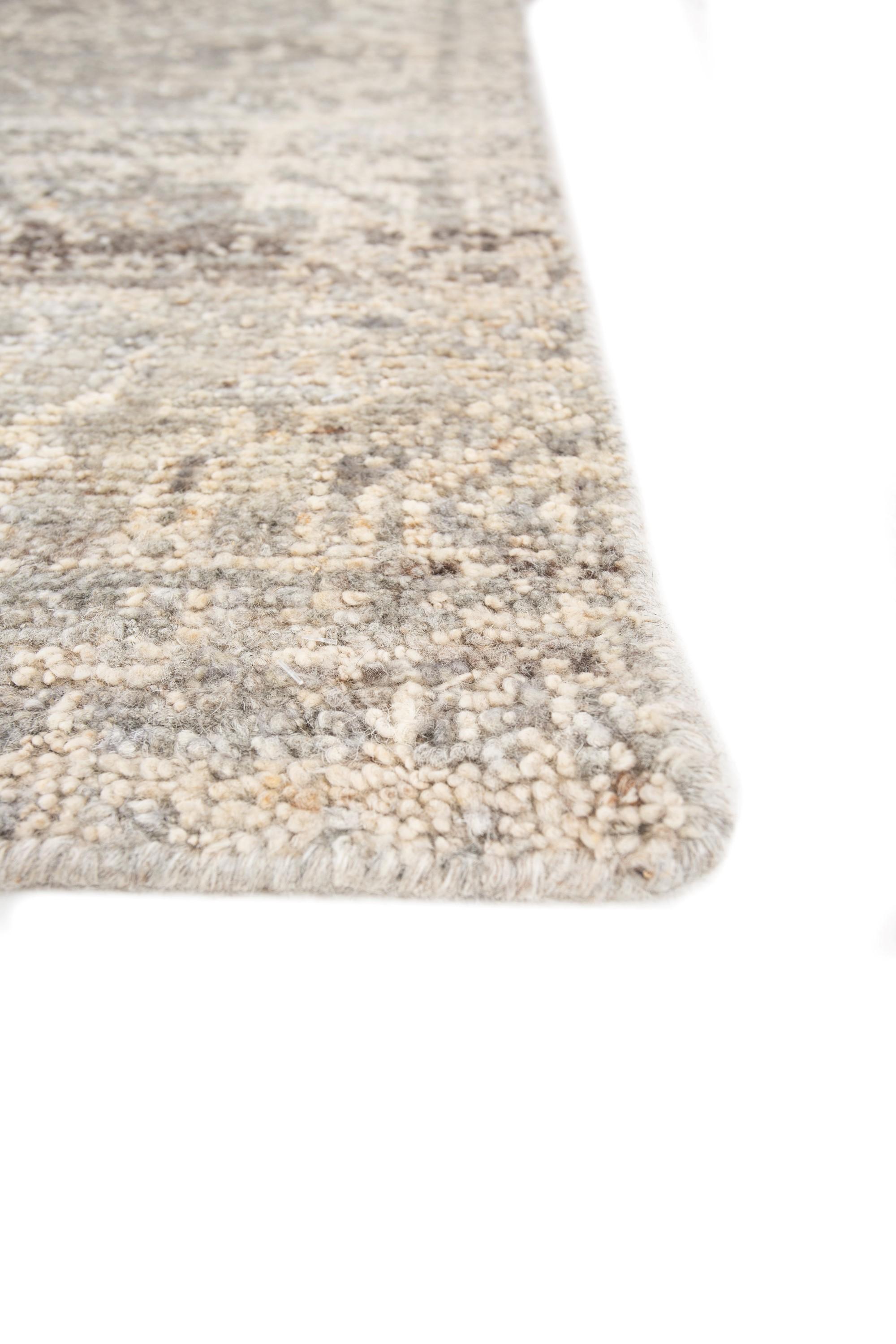 Step into a tapestry of timeless elegance with our hand-knotted rug, where wool and silk unite in a dance of luxury. The handmade rug drenched in natural gray, mirroring untouched landscapes, seamlessly blending with a border of the same serene