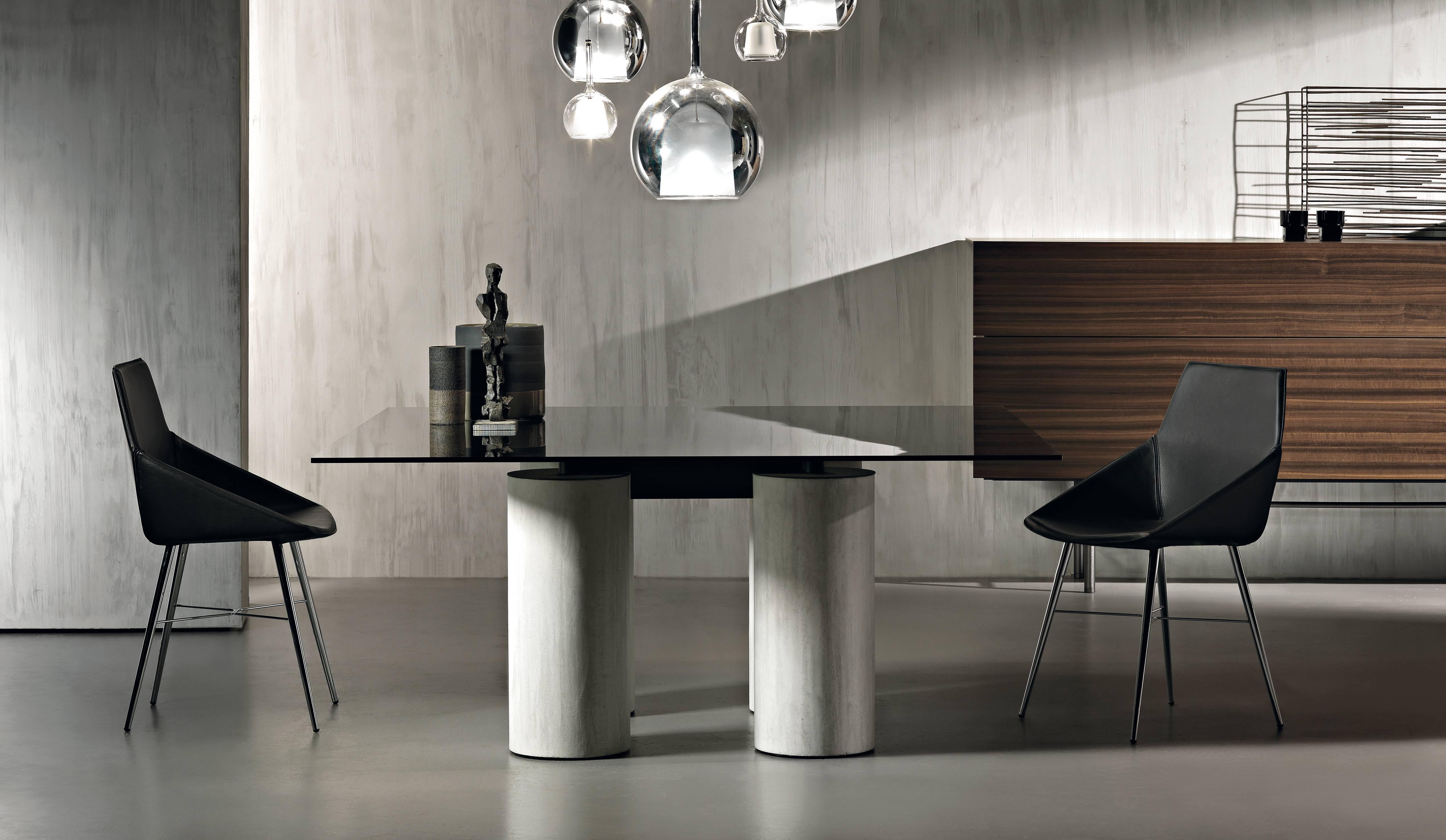 Table with a unique and timeless design in which the apparent thinness and lightness of the glass top contrasts with the considerable diameter of the columns. These columns acquire greater expressive force from the different colors and textures of