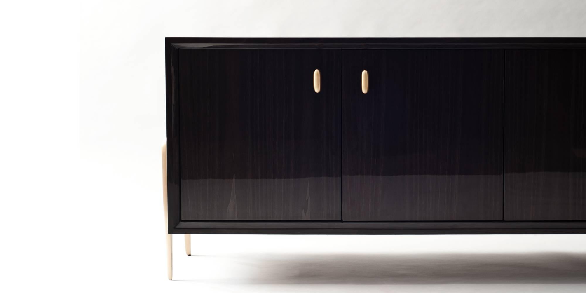 The Serge cabinet by DeMuro Das has a clean-lined body veneered in glossy dark grey dyed Tulipwood, an unusual species with a straight, finely-textured grain. The sculptural legs are mounted from each side of the cabinet and have been hand-cast in