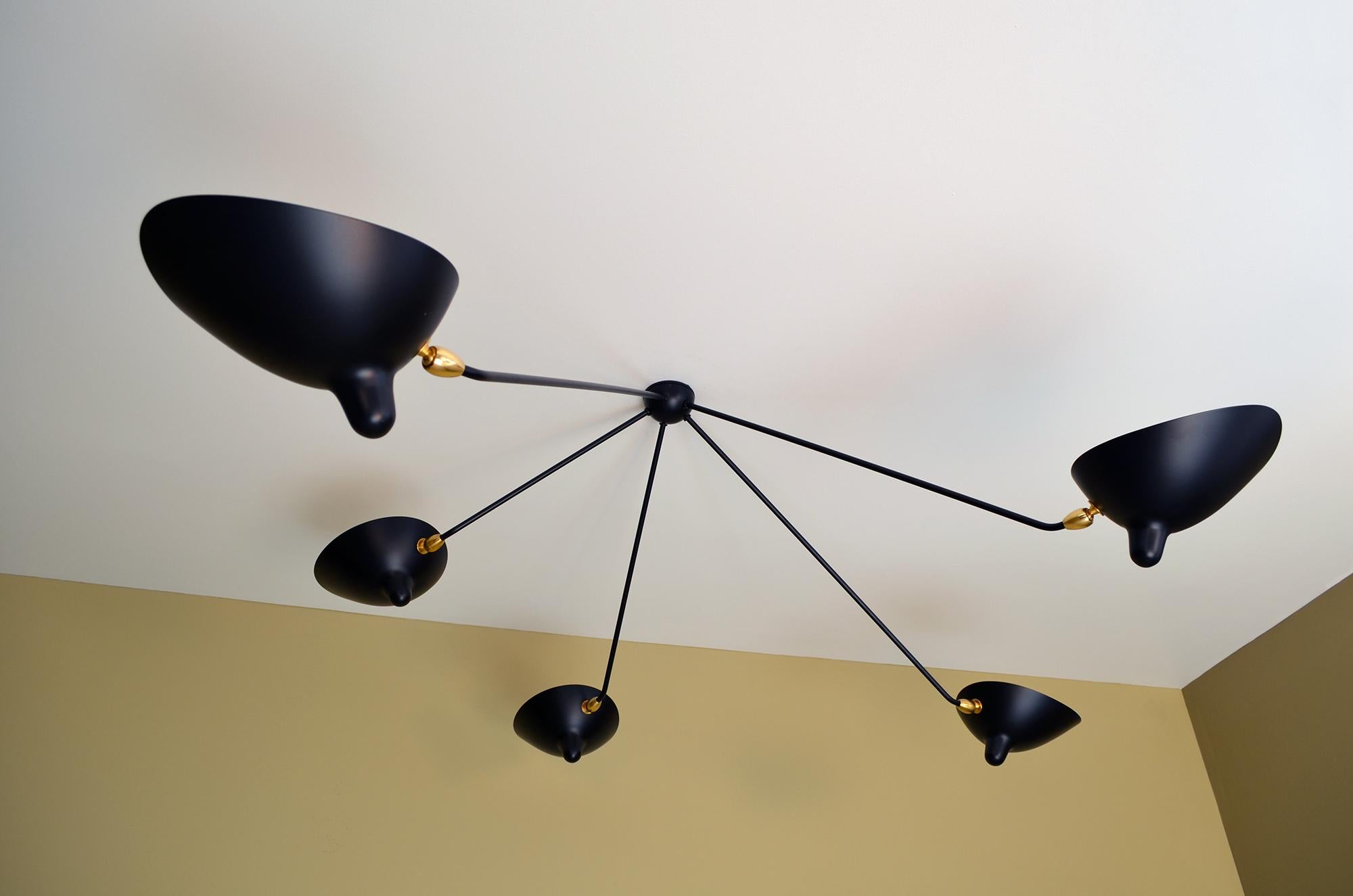 Elegance in form and function are hallmarks of a Serge Mouille lamp. This ceiling lamp with adjustable shades on five fixed arms is at once an old and practical design that works well as a primary light source. 

Brass swivels connect the