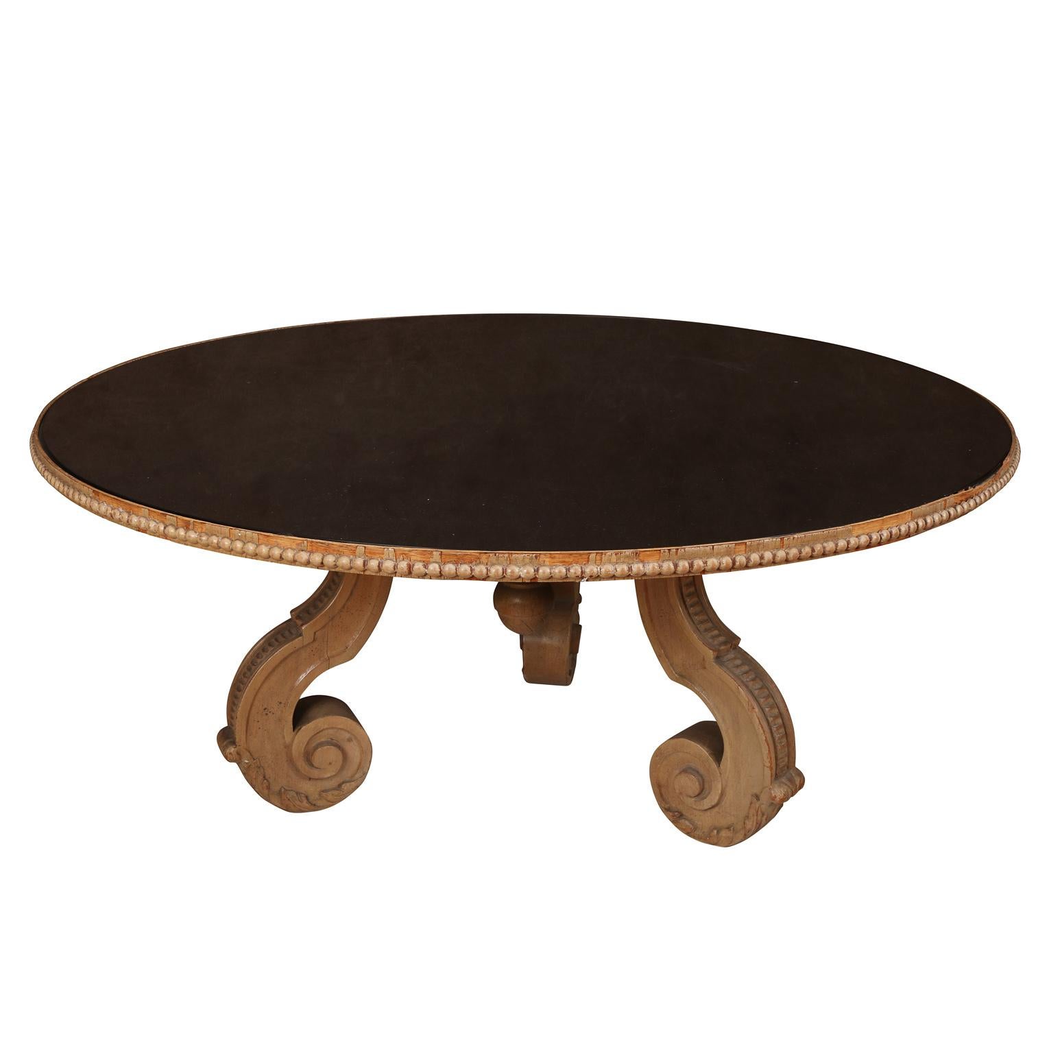 A beautiful and super chic vintage round coffee table with black mirrored top and carved wood base with Serge Roche inspired detail.