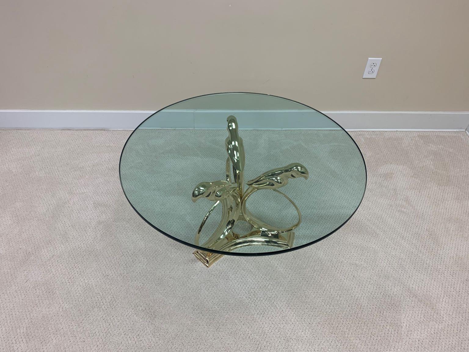 Brass and glass cocktail table attributed to Sergio Bustamante. Incredible table with a base of three parrots all in solid brass with a three-quarter inch glass top. The brass has been beautifully and professionally re-polished. The original glass