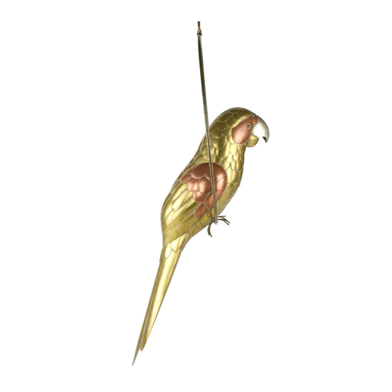 This large mixed metal figural parrot was designed by highly regarded Mexican sculptor Sergio Bustamante. The hand crafted bird is composed of brass, copper and steel and features glass eyes. The parrot has been posed as if clutching a large