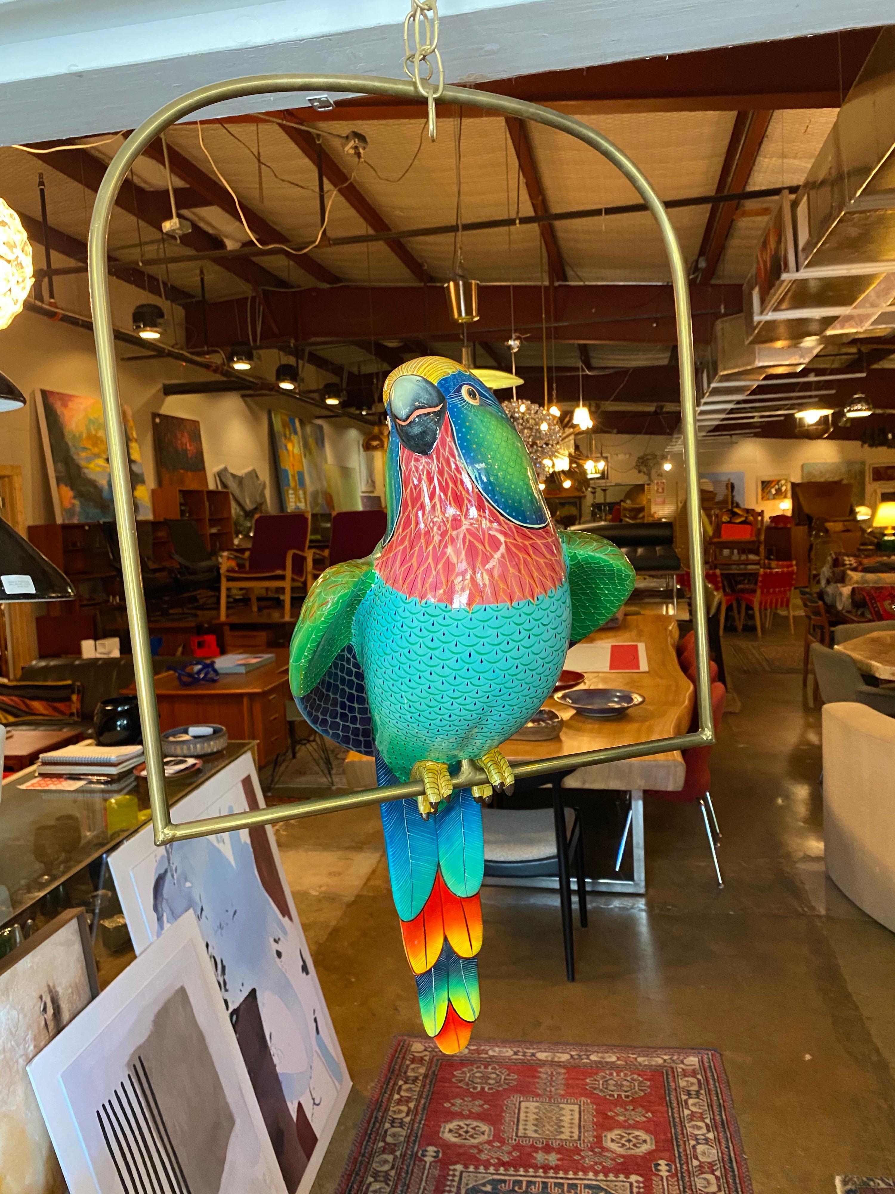 Beautiful papier mâché parrot by Mexican artist Sergio Bustamante. Brightly colored, the parrot sits on a hanging brass perch. Sergio Bustamante is known for his animal sculptures using a variety of mediums such as brass, metal, ceramic and, papier