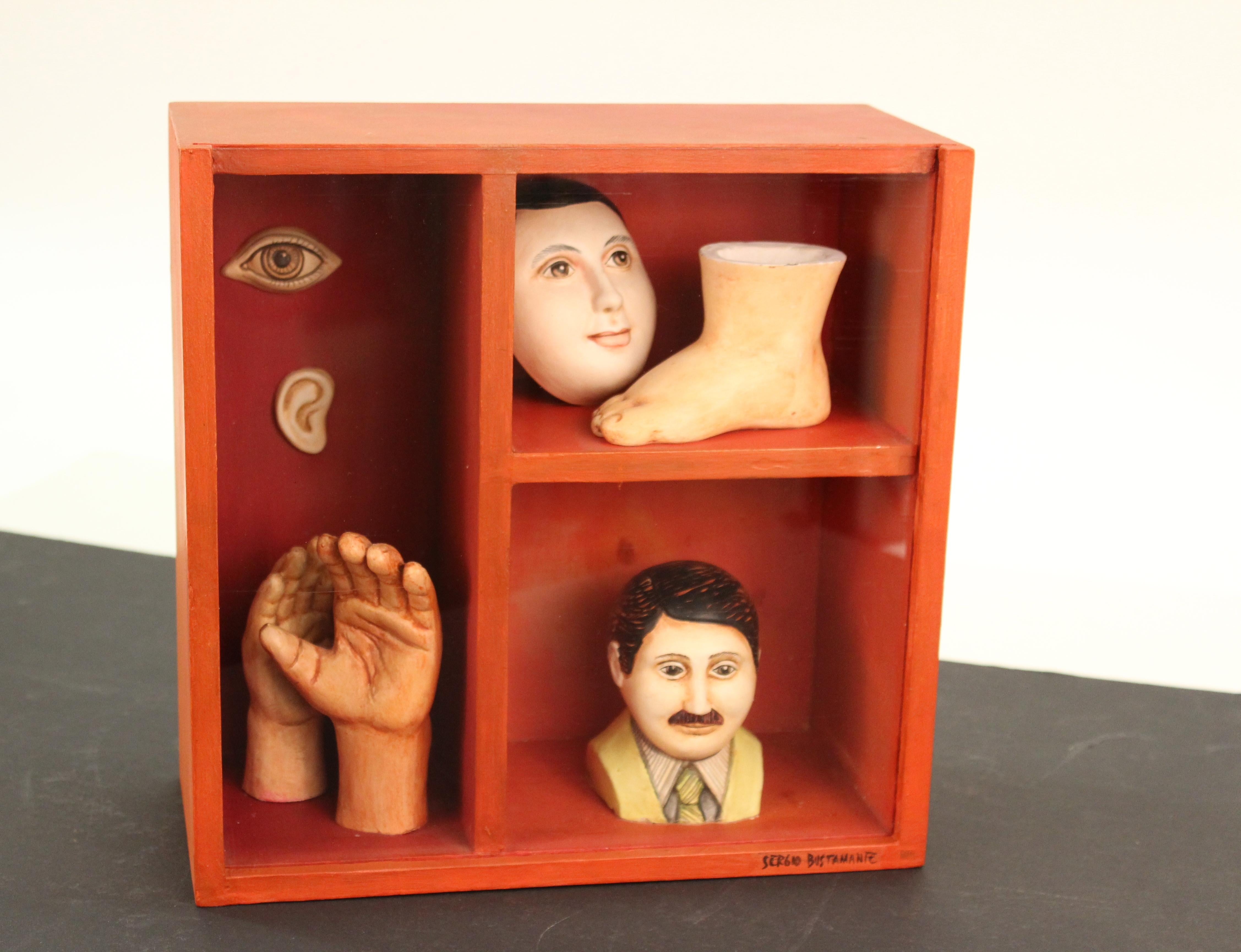 Sergio Bustamante (Mexican, Born 1942) surrealist-style sculpture of a shadow box in red wood with several cubby spaces. Each space contains a part of the human body including a foot, a pair of hands, and eye, an ear and two human busts; one of