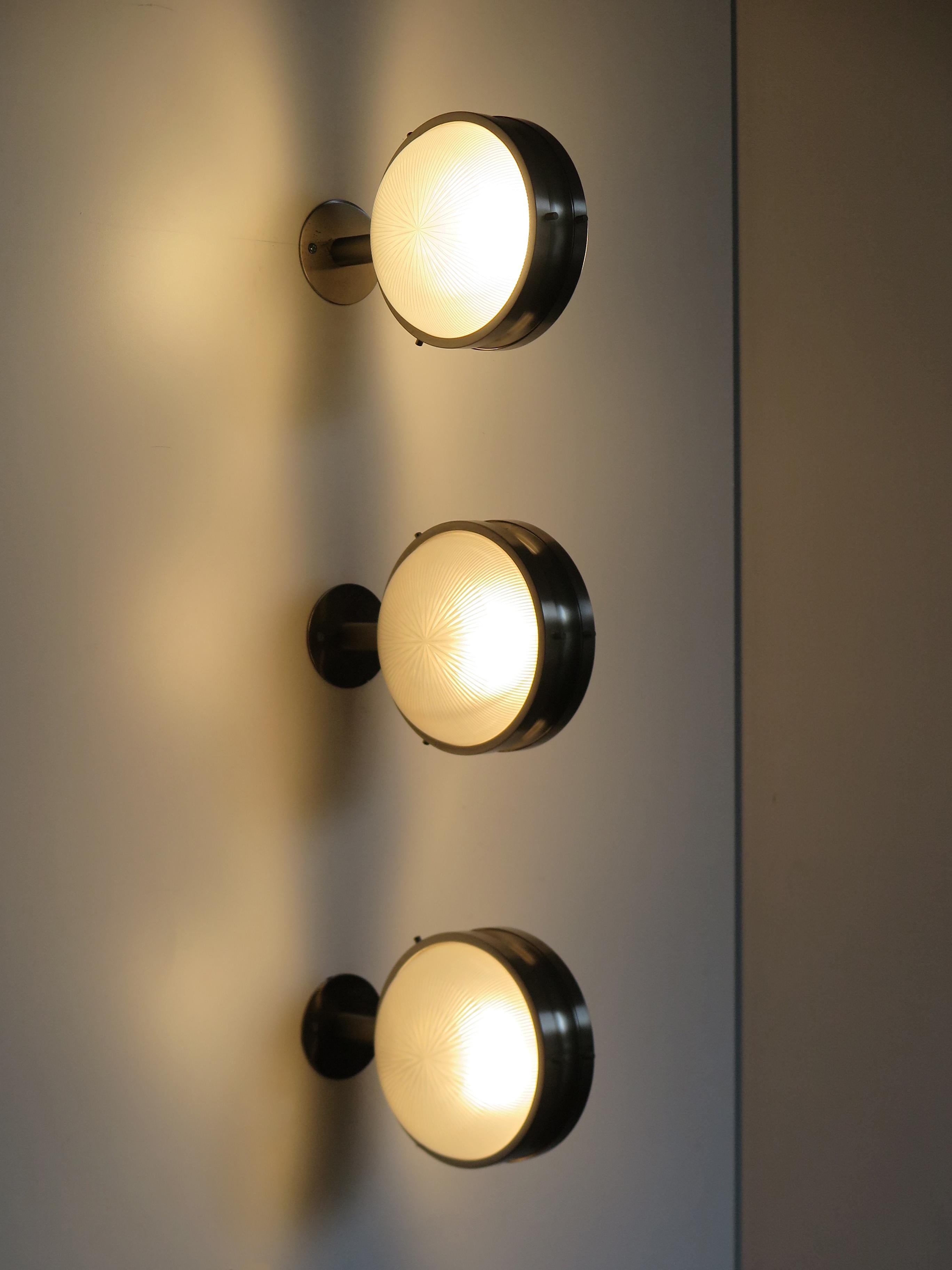 Italian set of three Mid-Century Modern design sconces wall lamps from the Gamma series designed by Sergio Mazza and produced by Artemide with brushed steel frame and thick molded glass diffusers, Italy 1960s.

The wall sconces can be mounted