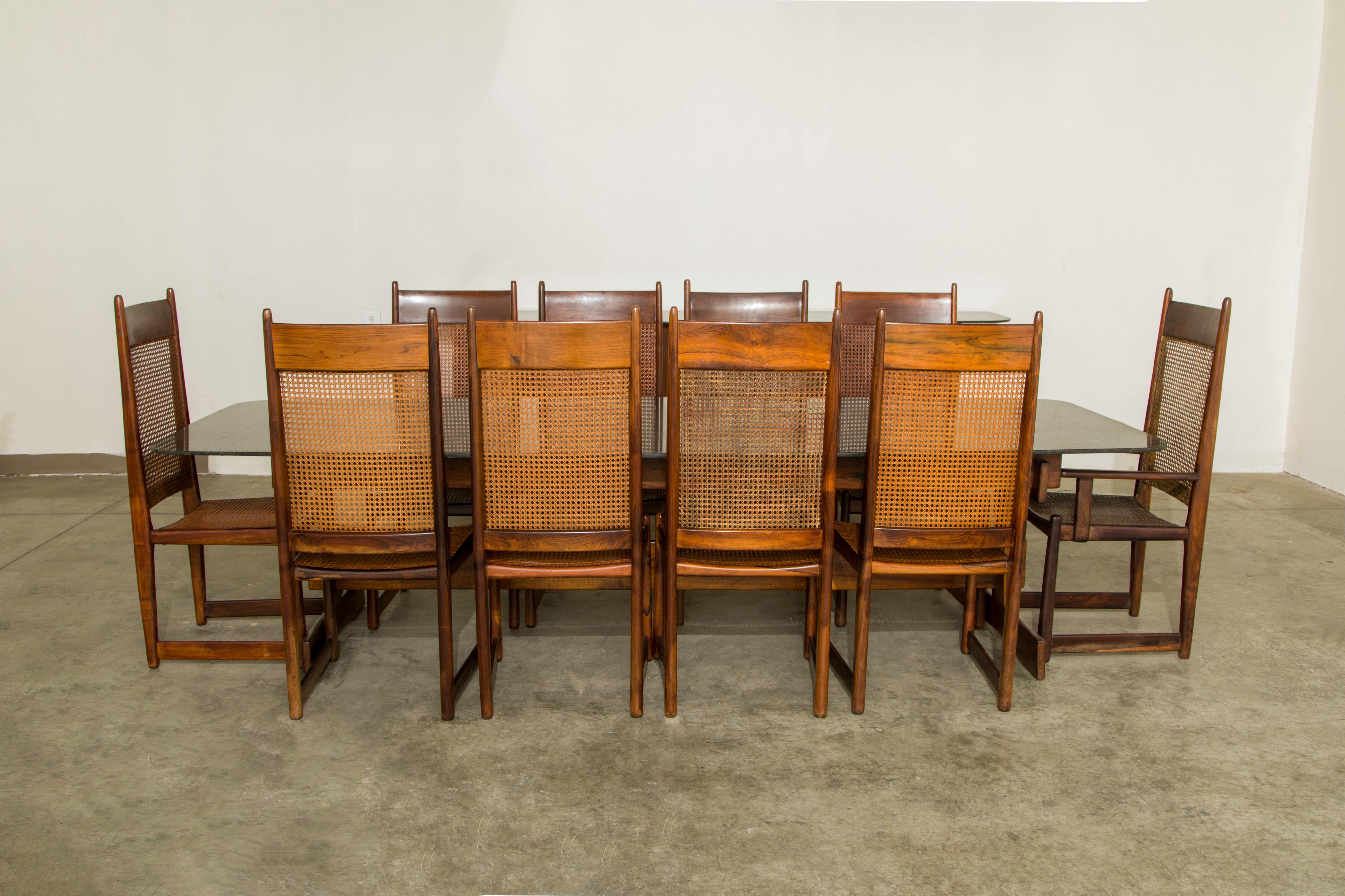 This monumental and important 1960s Jacaranda Rosewood dining set by Sergio Rodrigues in collaboration with architect Bernardo Figuiredo includes a granite topped trestle base dining table and ten (10) caned dining chairs. For the ultimate in